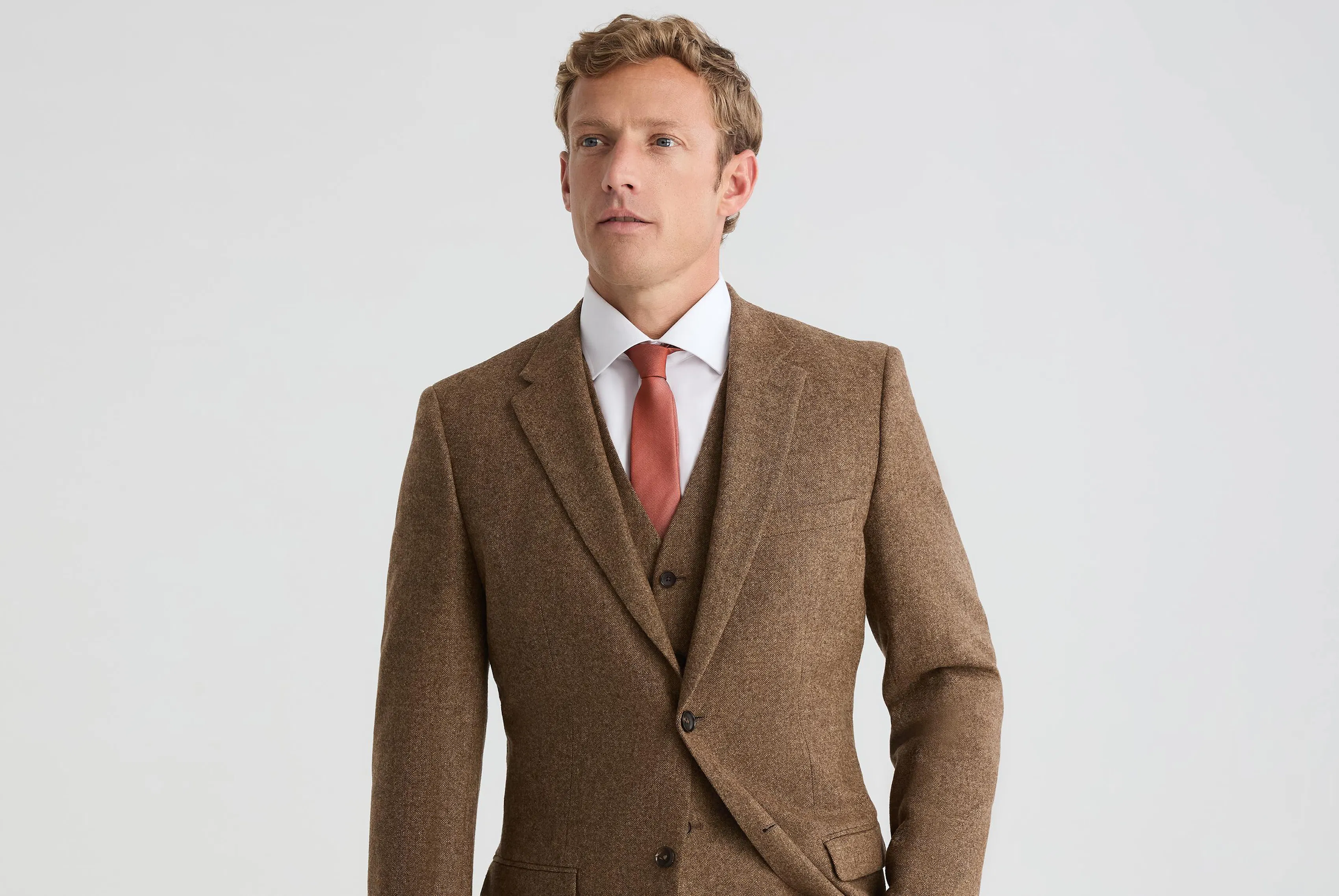 Man wearing a brown three-piece suit with a white dress shirt and rust-colored tie for a fall wedding look.