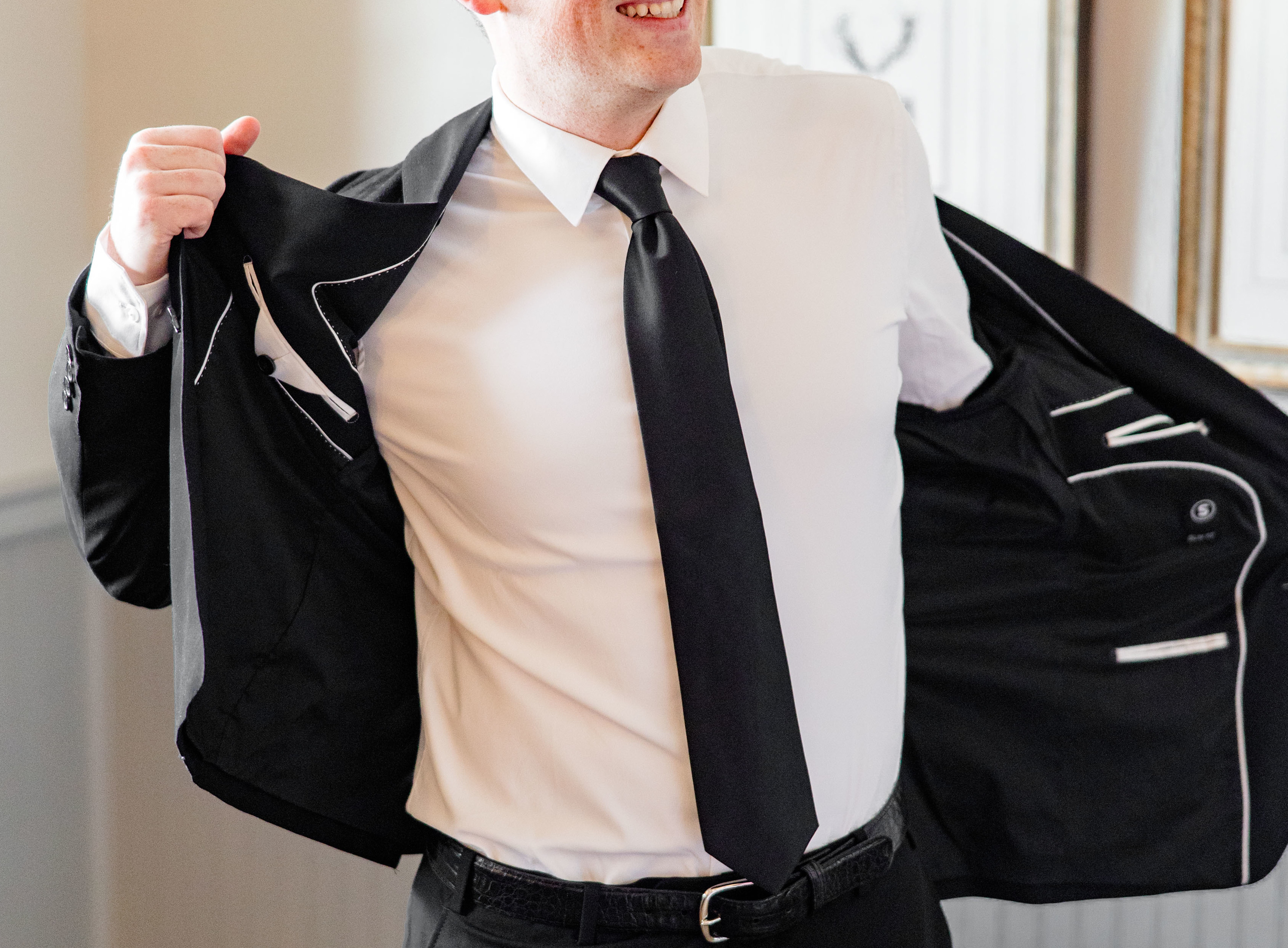 Groom wearing a black suit jacket with a white dress shirt and black tie.