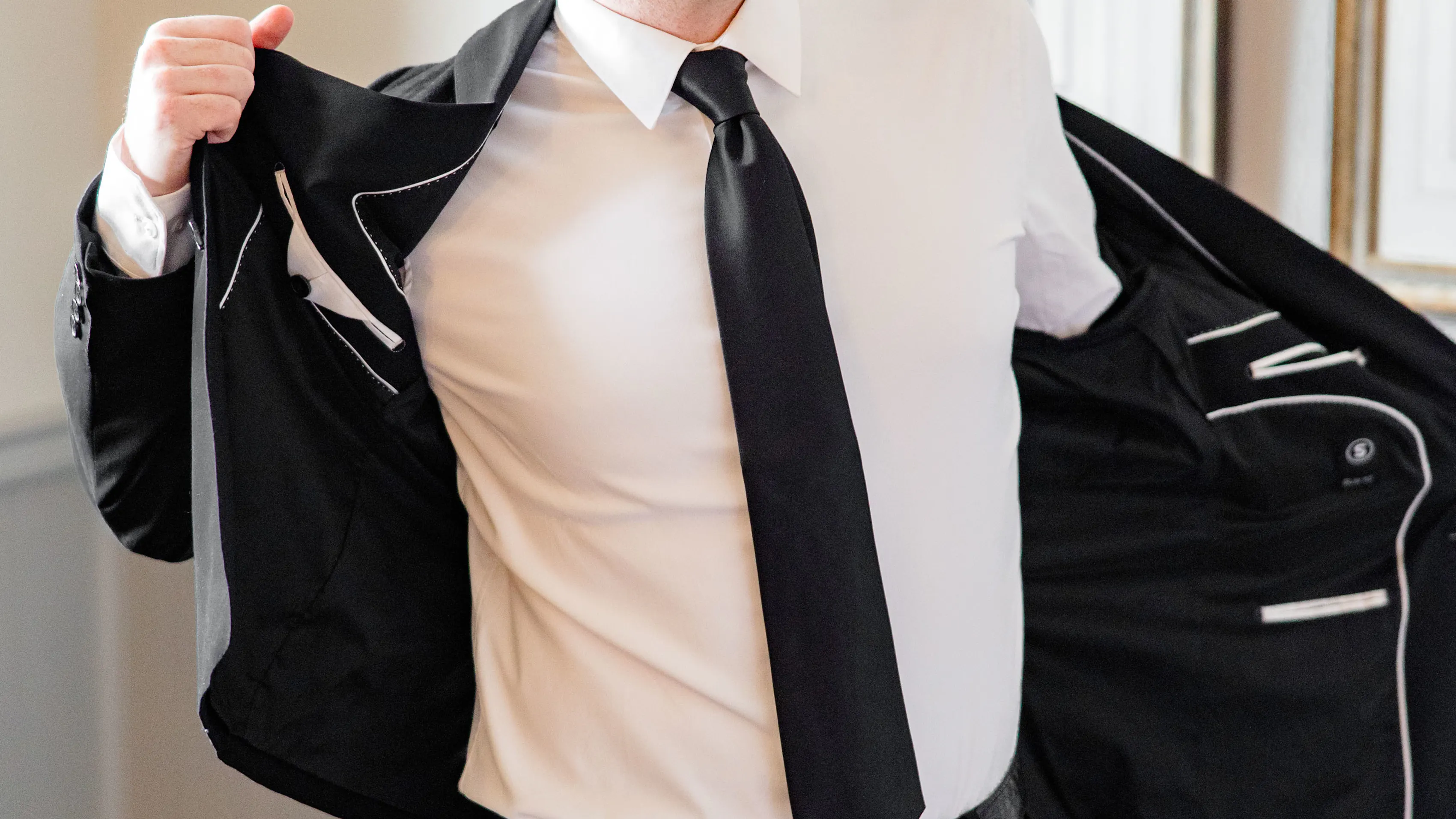 Groom wearing a black suit jacket with a white dress shirt and black tie.