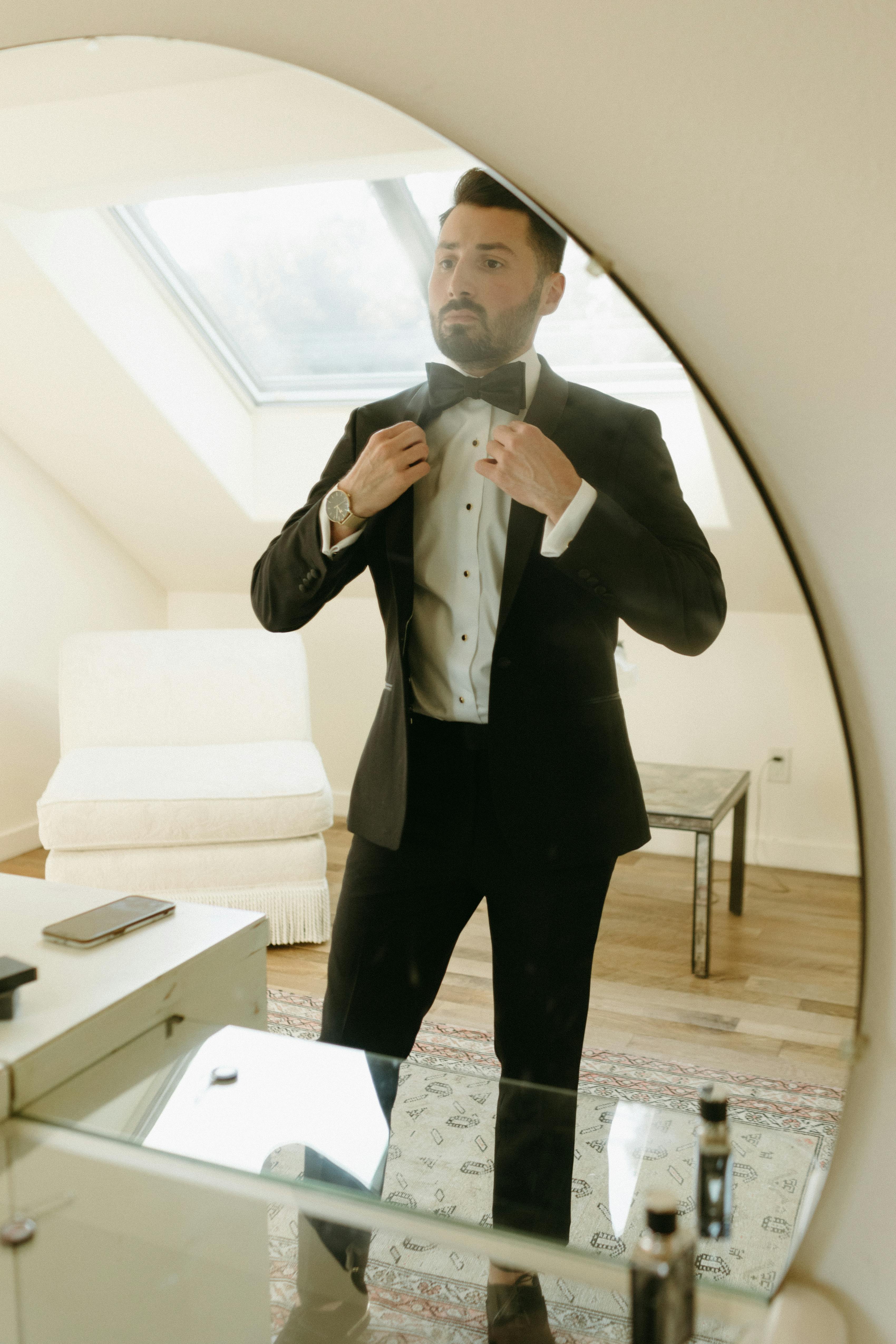 Man adjusting his bow tie waring black tuxedo for formal new year's eve party outfit