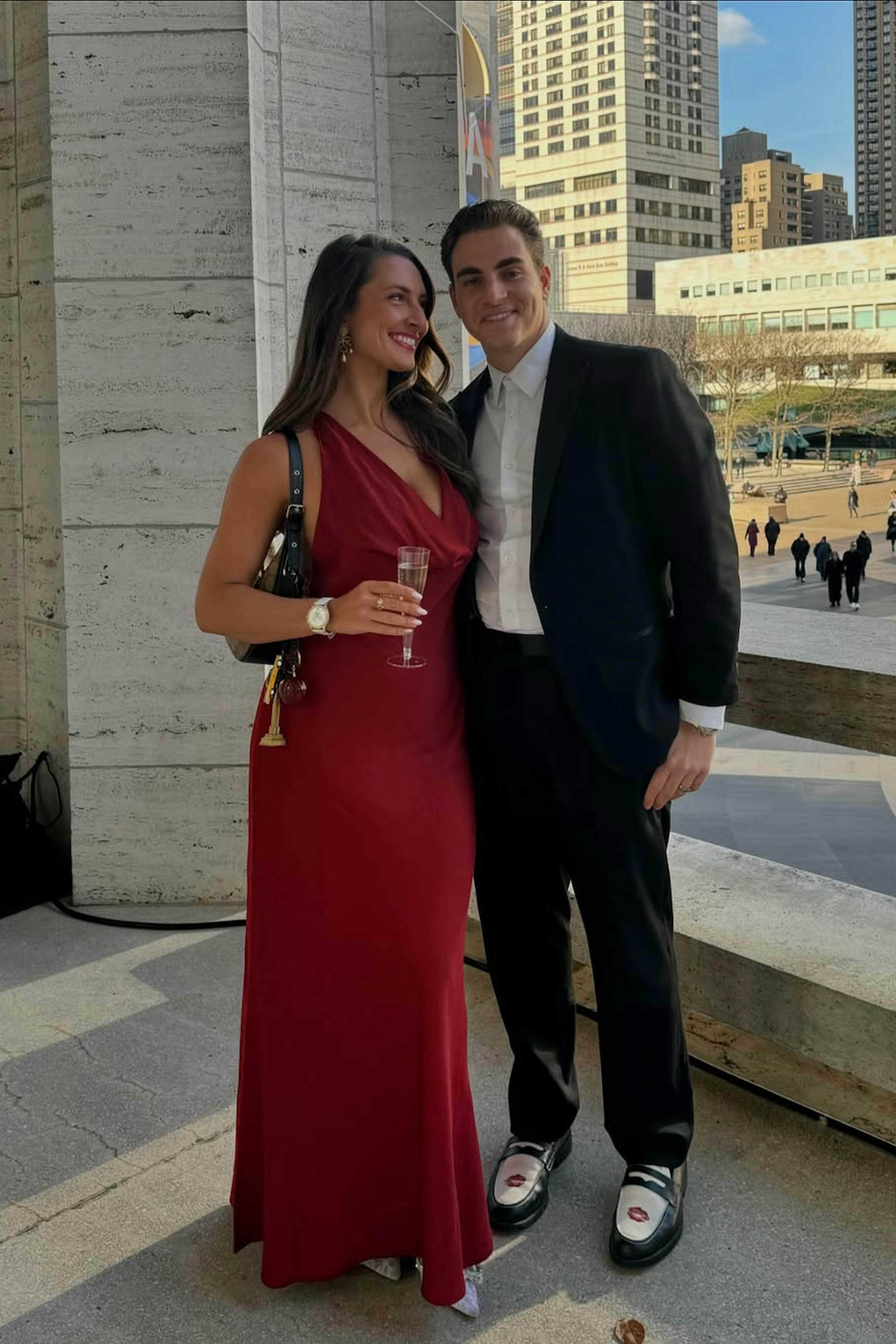 Couple wearing semi-formal winter wedding outfits in pink cowl neck gown and black suit with loafers