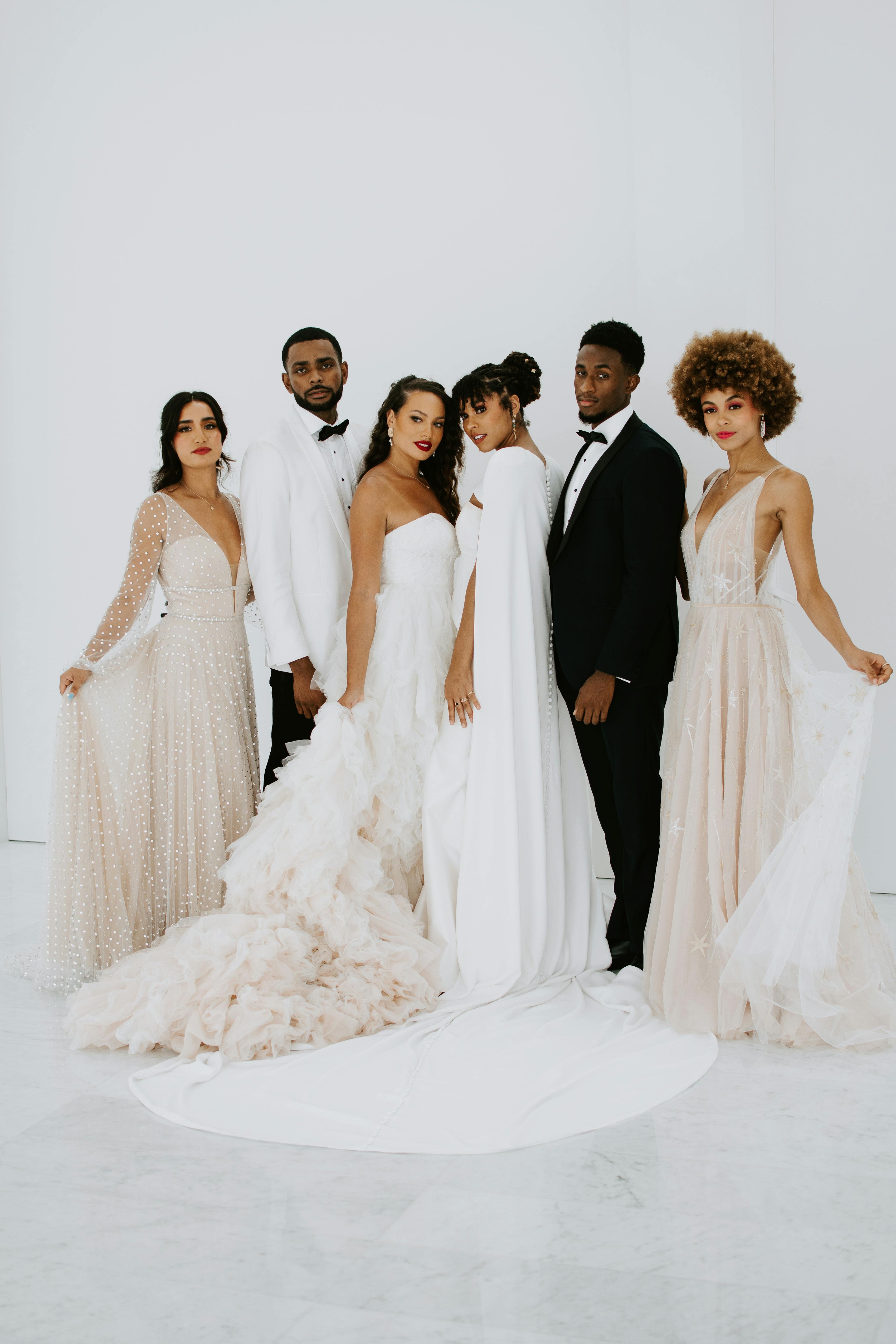 All-white wedding party attire with light pink, white, champagne, and black groomsman suits and bridesmaid dresses