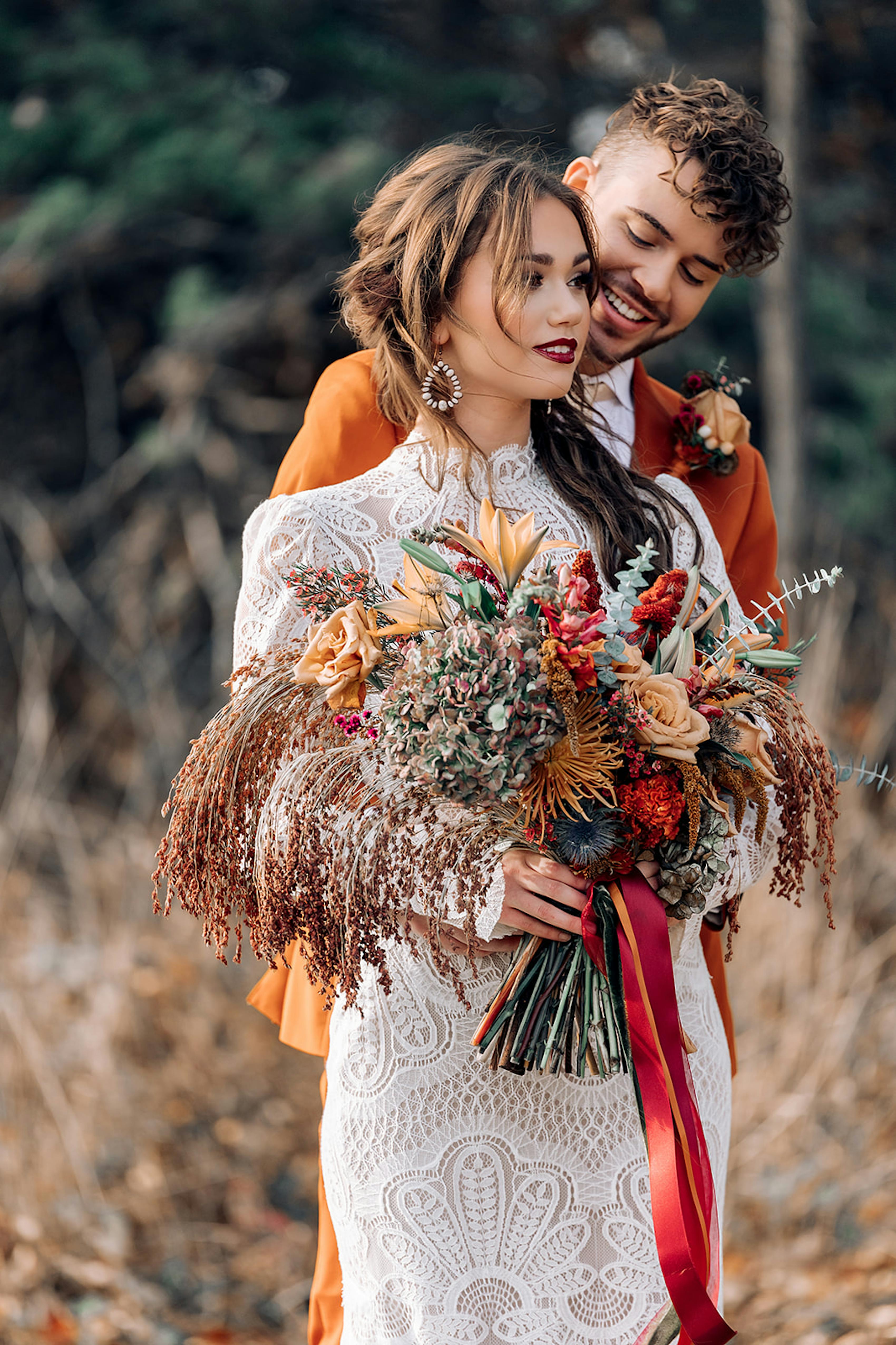 Lace wedding gown with wildflower wedding bouquet and burnt orange groom suit