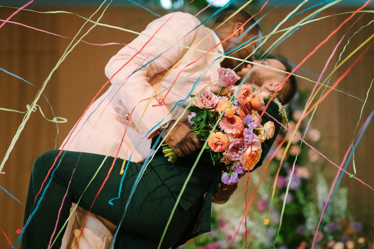 Grooms kissing under colorful wedding streamers for gay ceremony