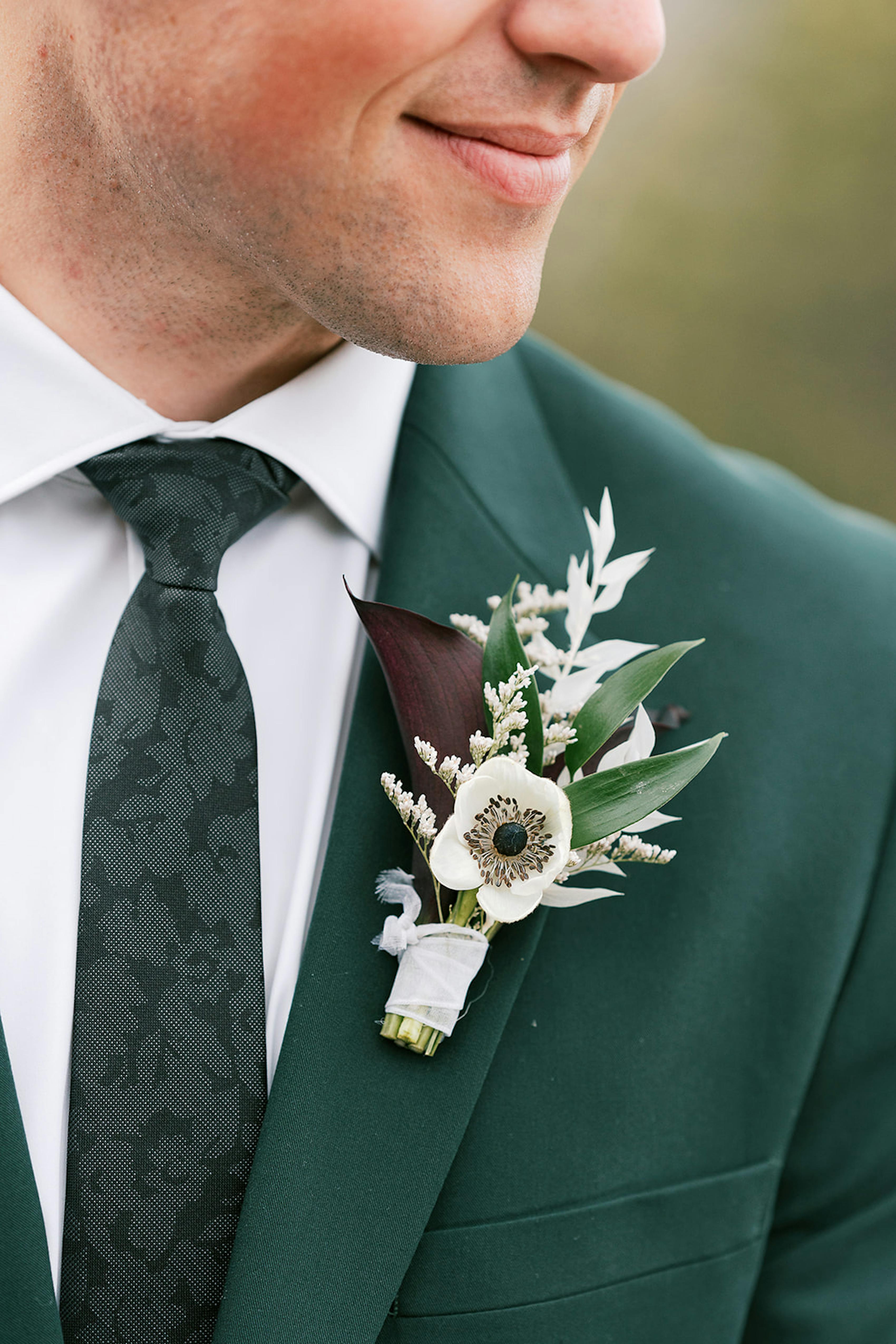 Dark green suit with dark purple and green boutonniere for earthy wedding theme