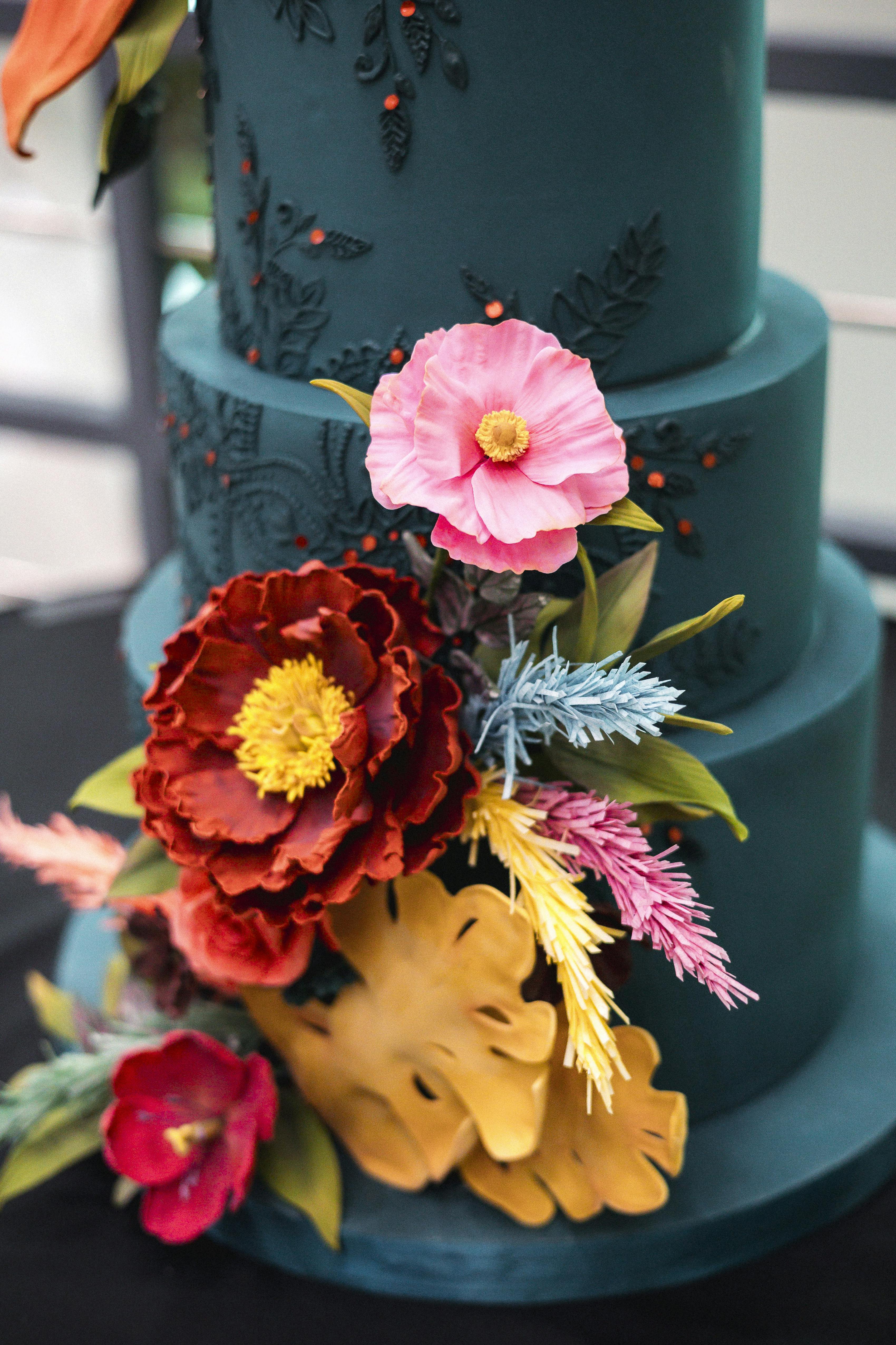 Teal and red wedding cake with bright flowers for unique, colorful palette