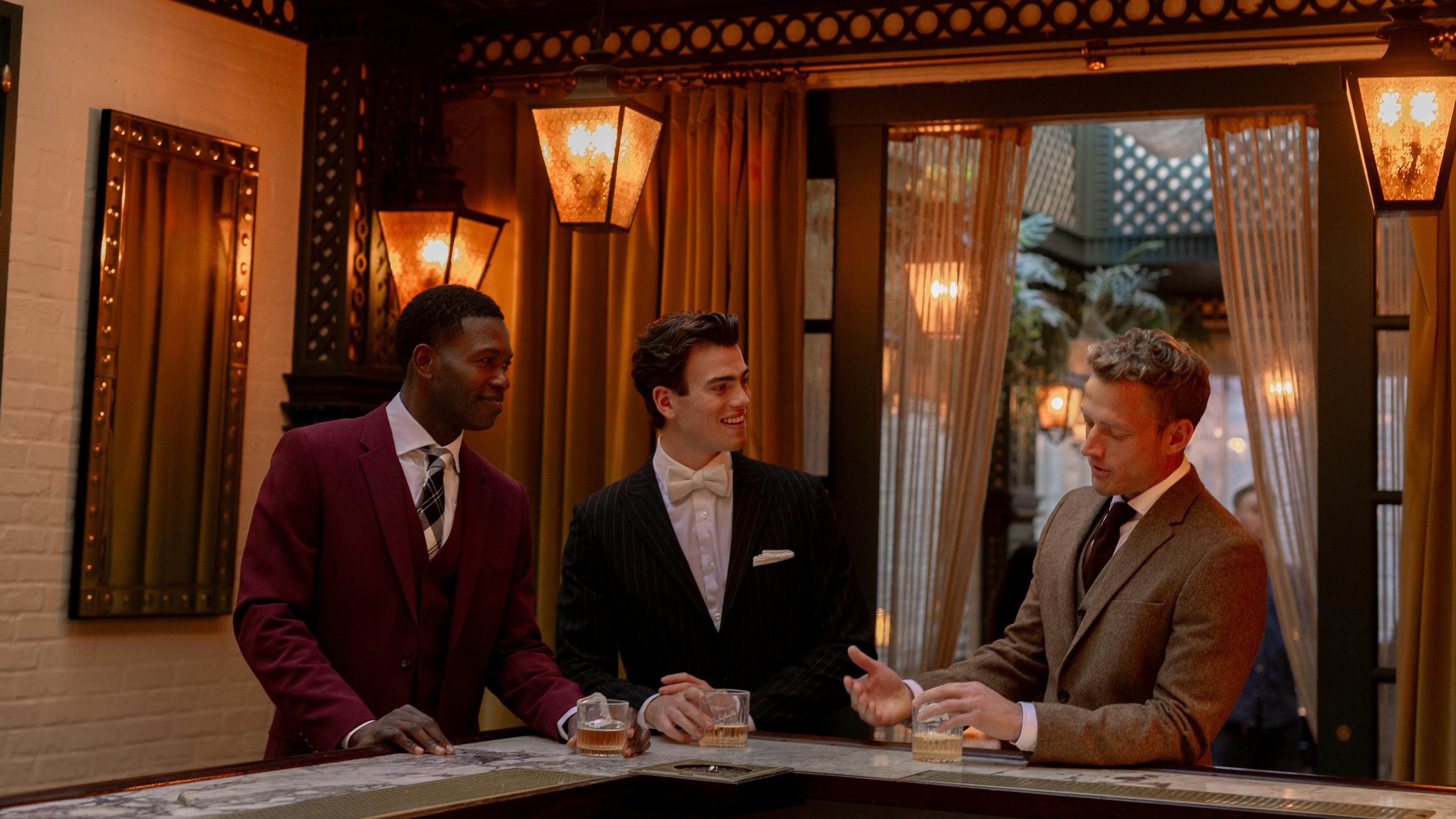 3 men at a bar in trendy suit style with merlot suit, black pinstripe suit, and tweed suit
