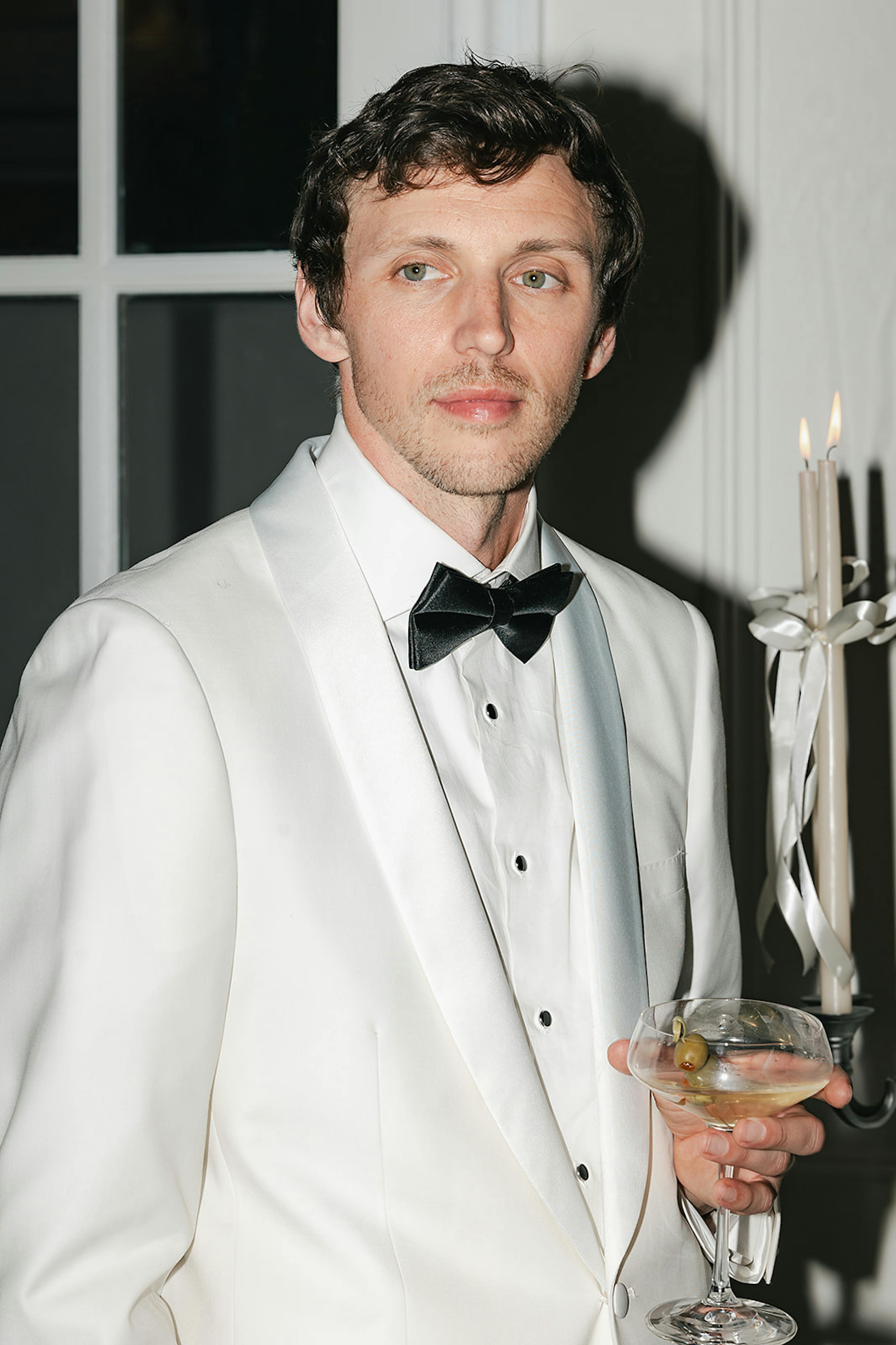 All white tuxedo groom holding glass of champagne at wedding reception