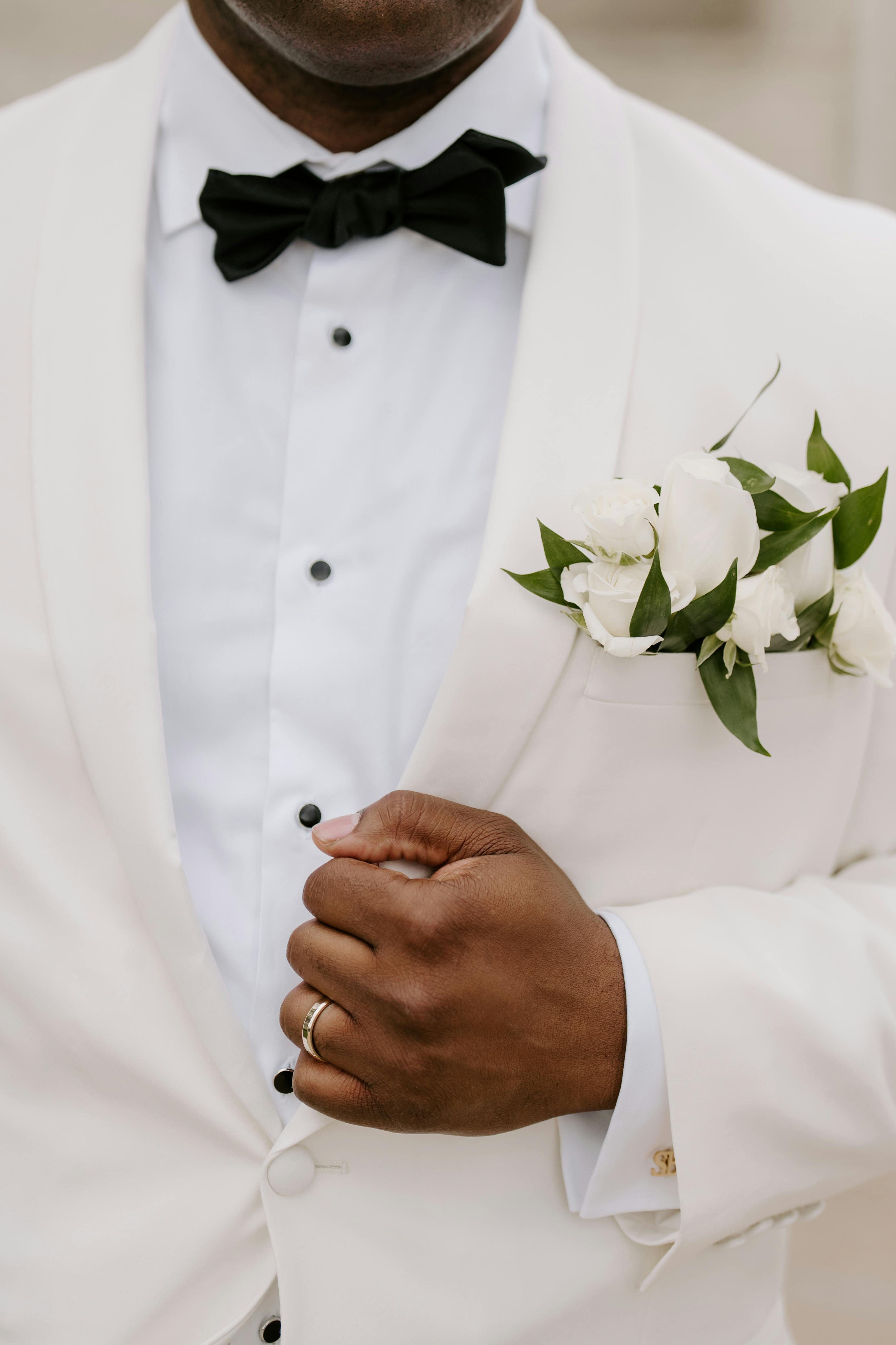 Groom wearing ivory tuxedo with white boutonniere walking down aisle