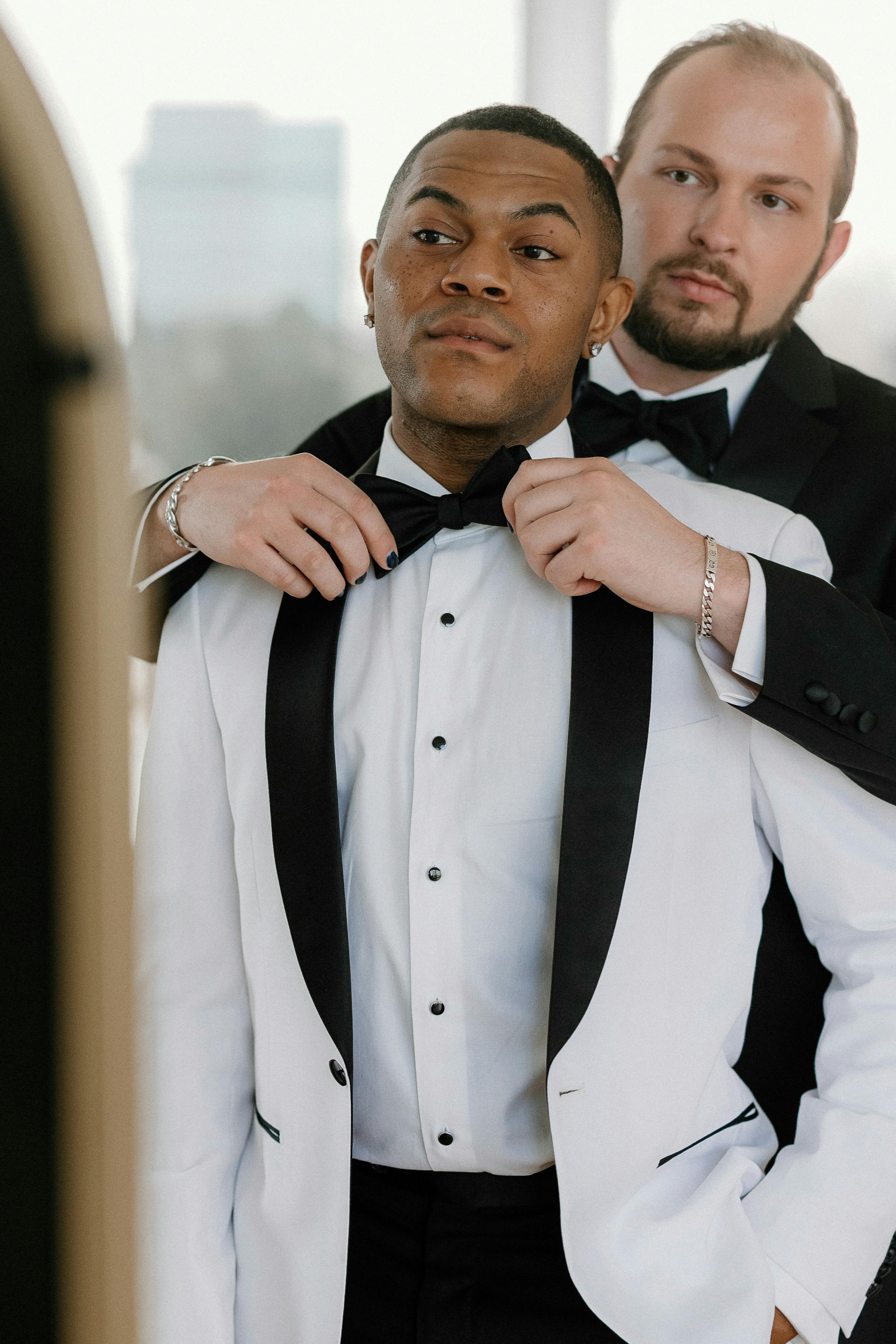 Gay wedding grooms wearing black and white tuxedos together getting ready