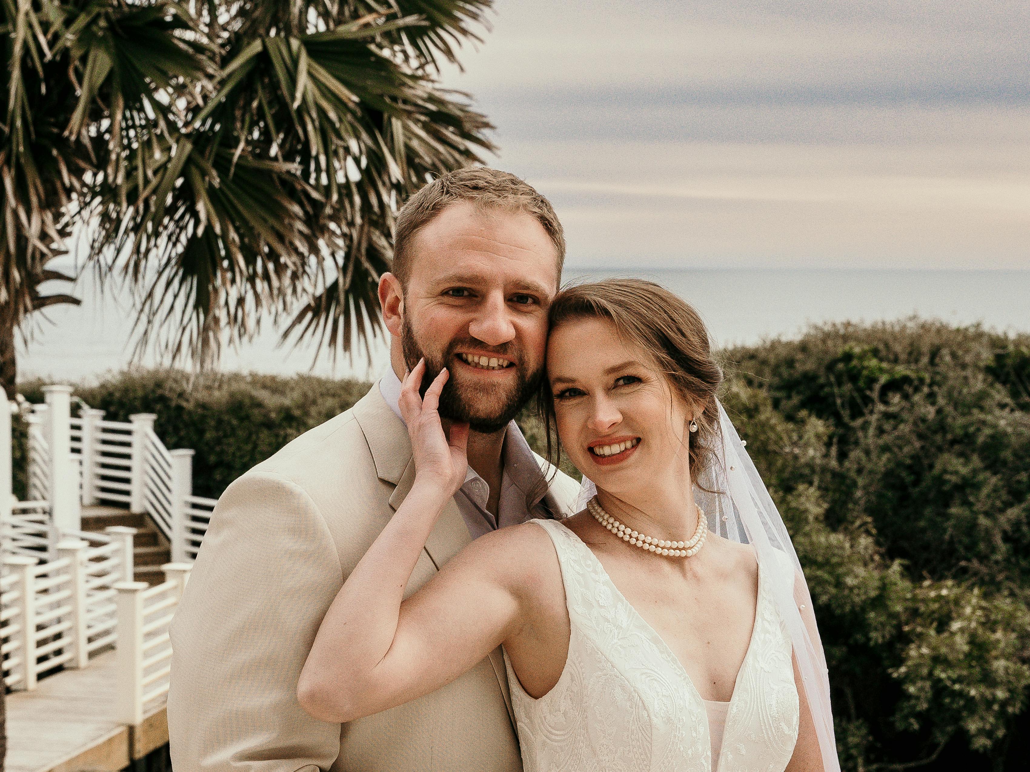 Groom in tan suit next to bride in white dress in front of a swimming pool at a destination wedding