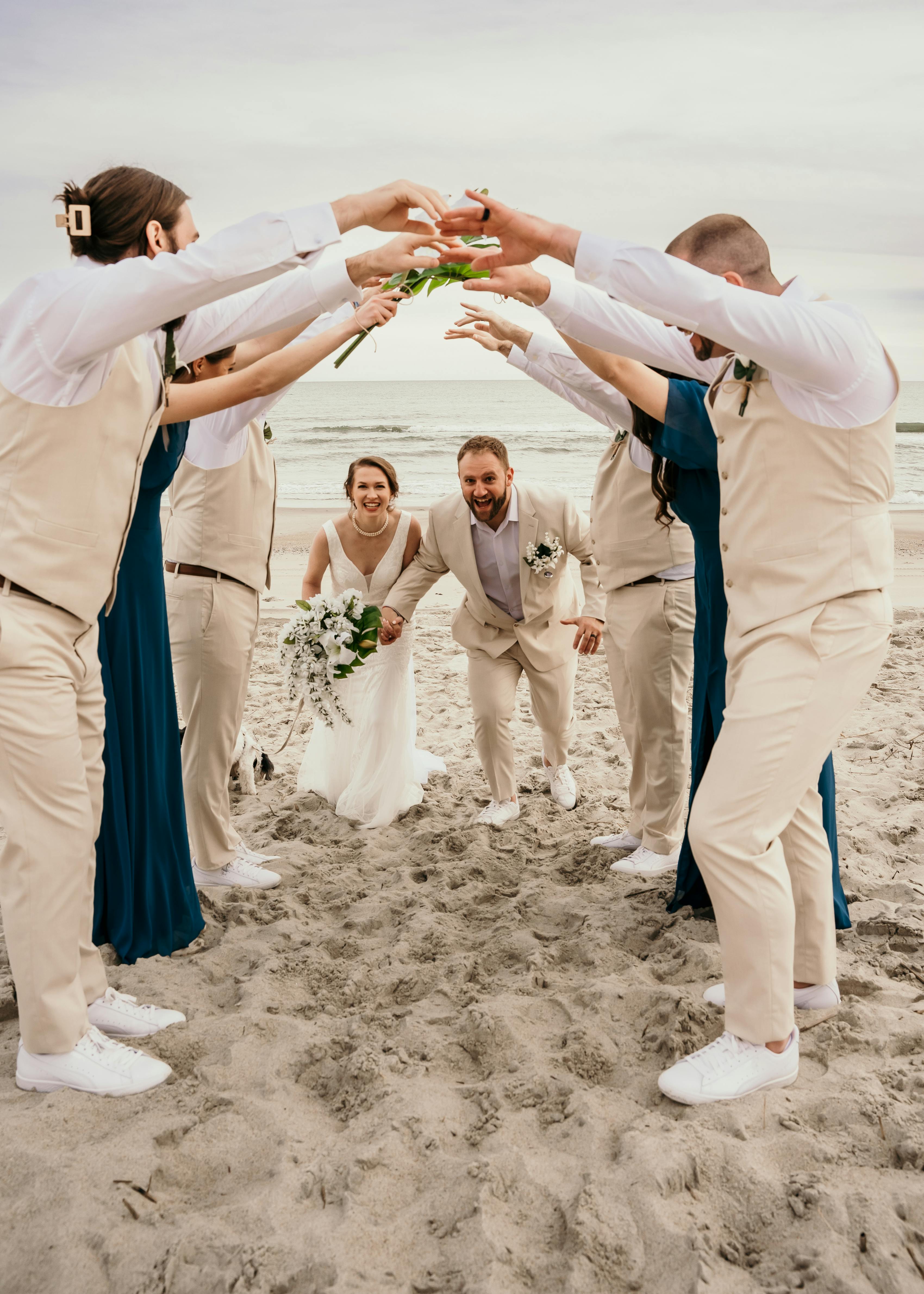 beach wedding party with groomsmen in tan suits and bridesmaids in navy blue dresses