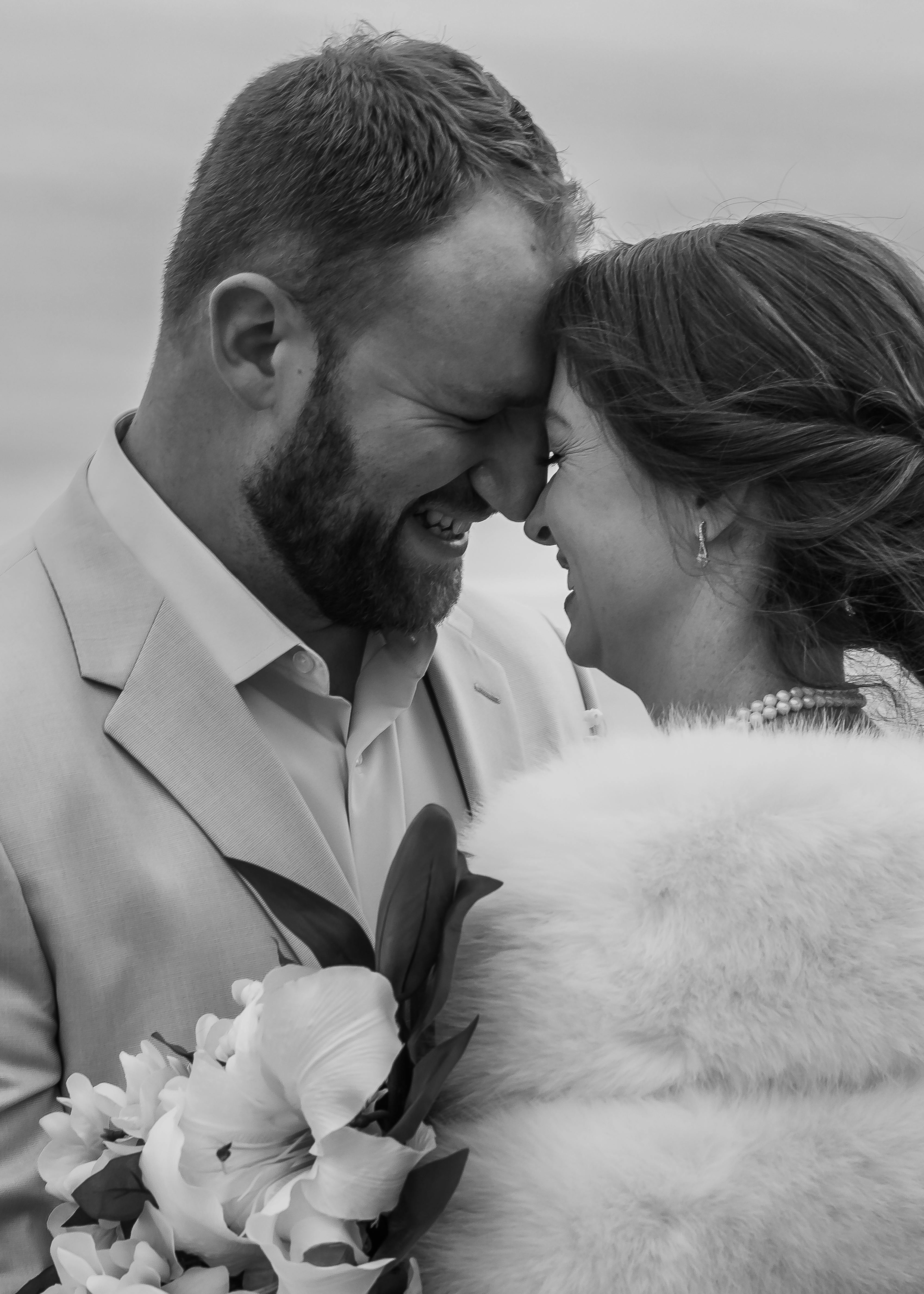 black and white photo of bride wearing a fur wedding shawl and groom in a light tan wedding suit
