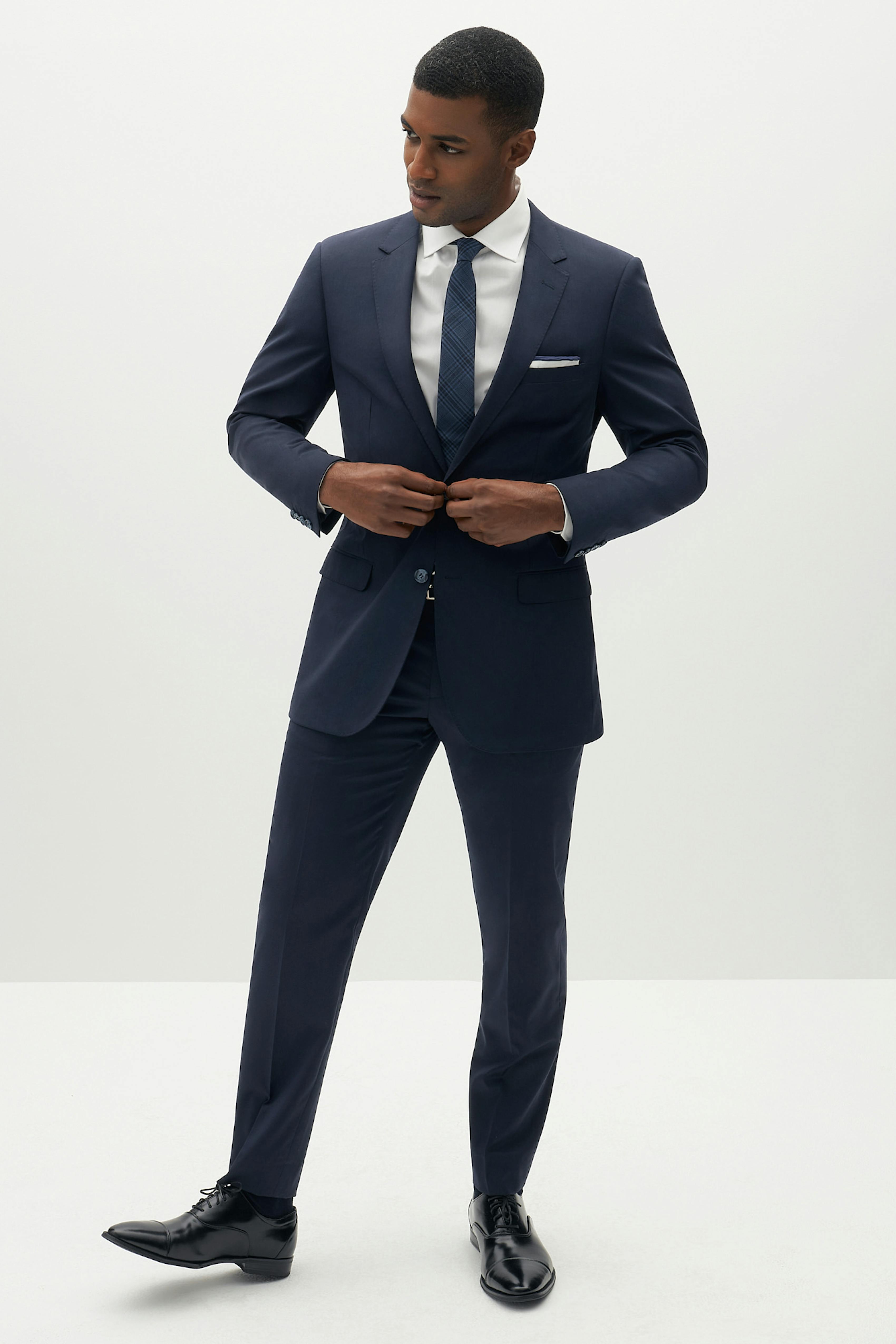 Men's navy suit with black shoes, black belt, and navy tie