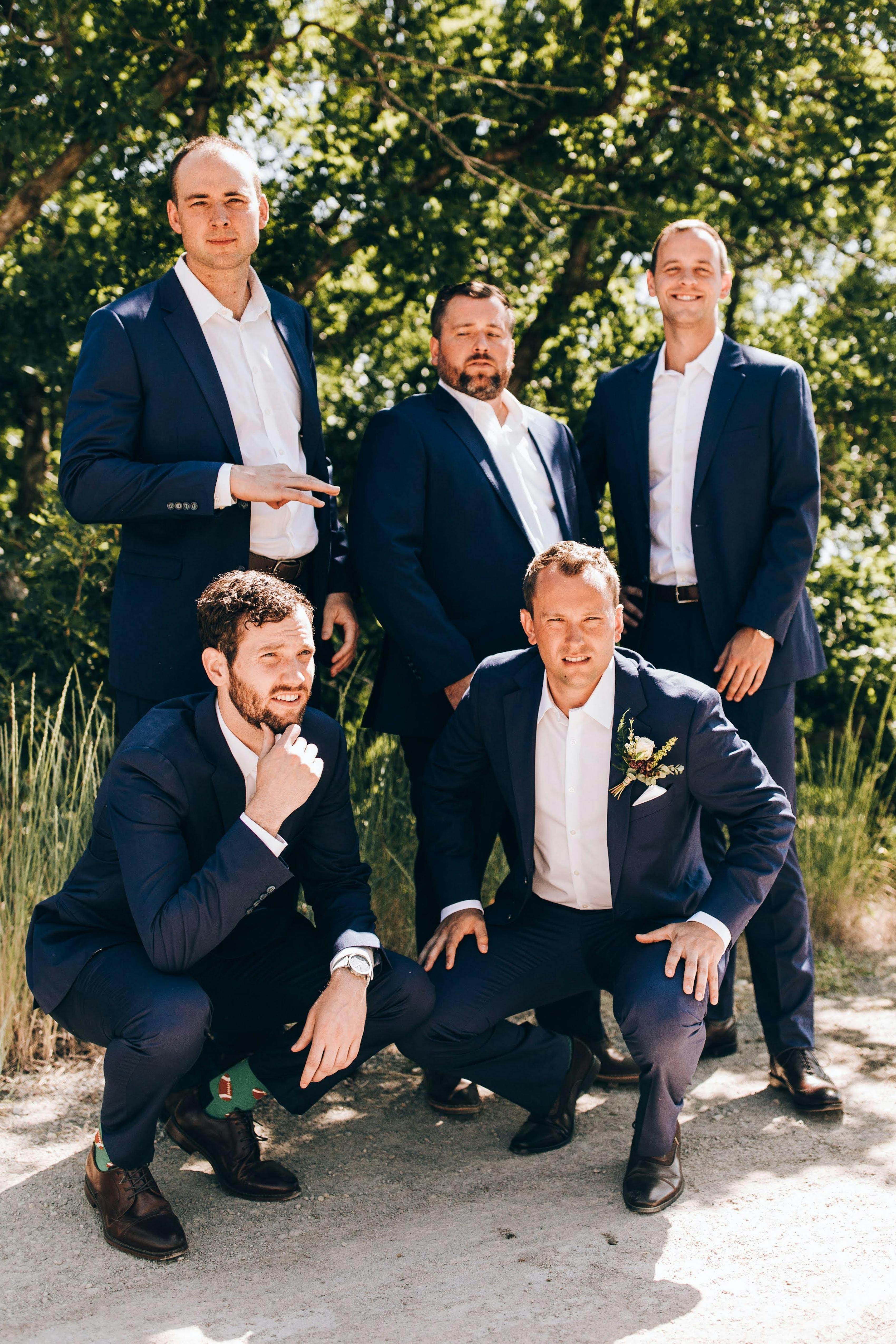 Groomsman group kneeling in men's navy suits with black shoes