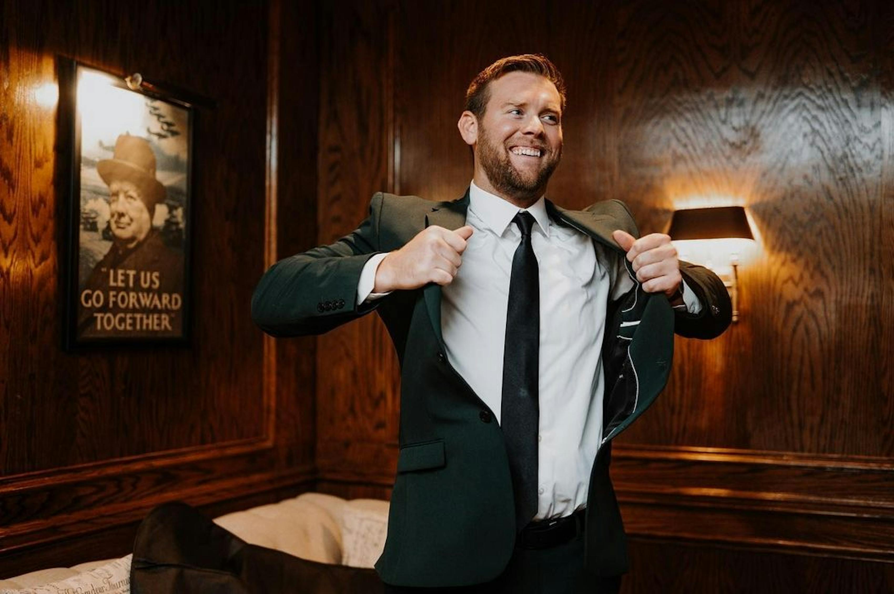 Putting on men's dark green suit jacket with black suit accessories getting ready for cocktail party