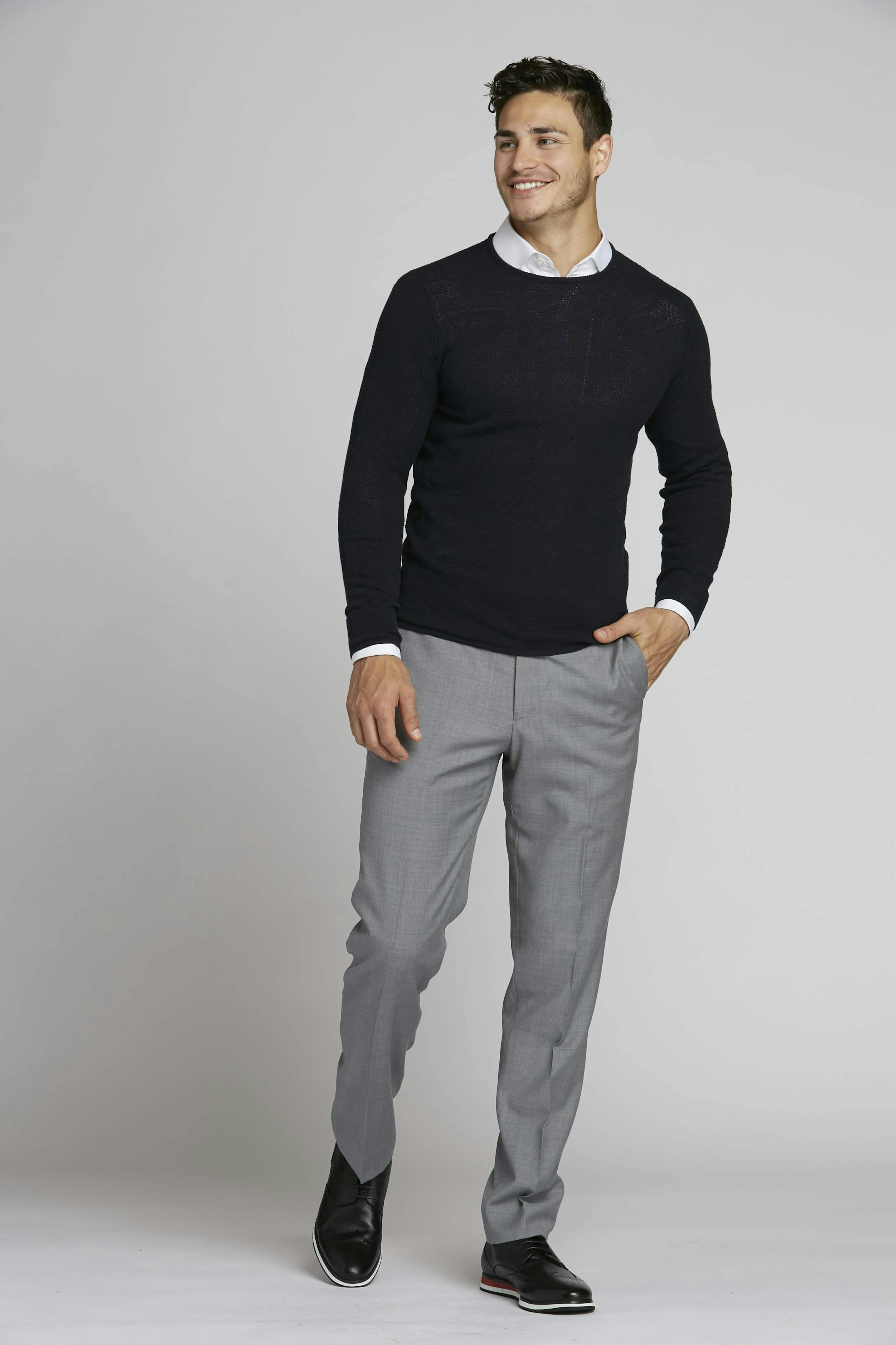Professional men's outfit with sweater, button-up shirt, and light grey slacks.