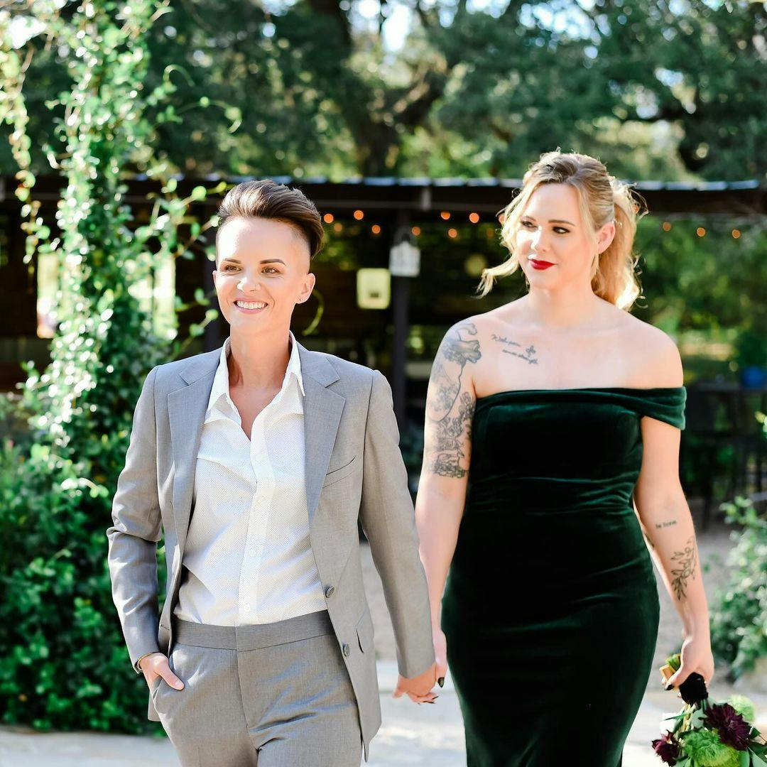 Two women at a wedding wearing a light grey women's suit and a green velvet one shoulder dress