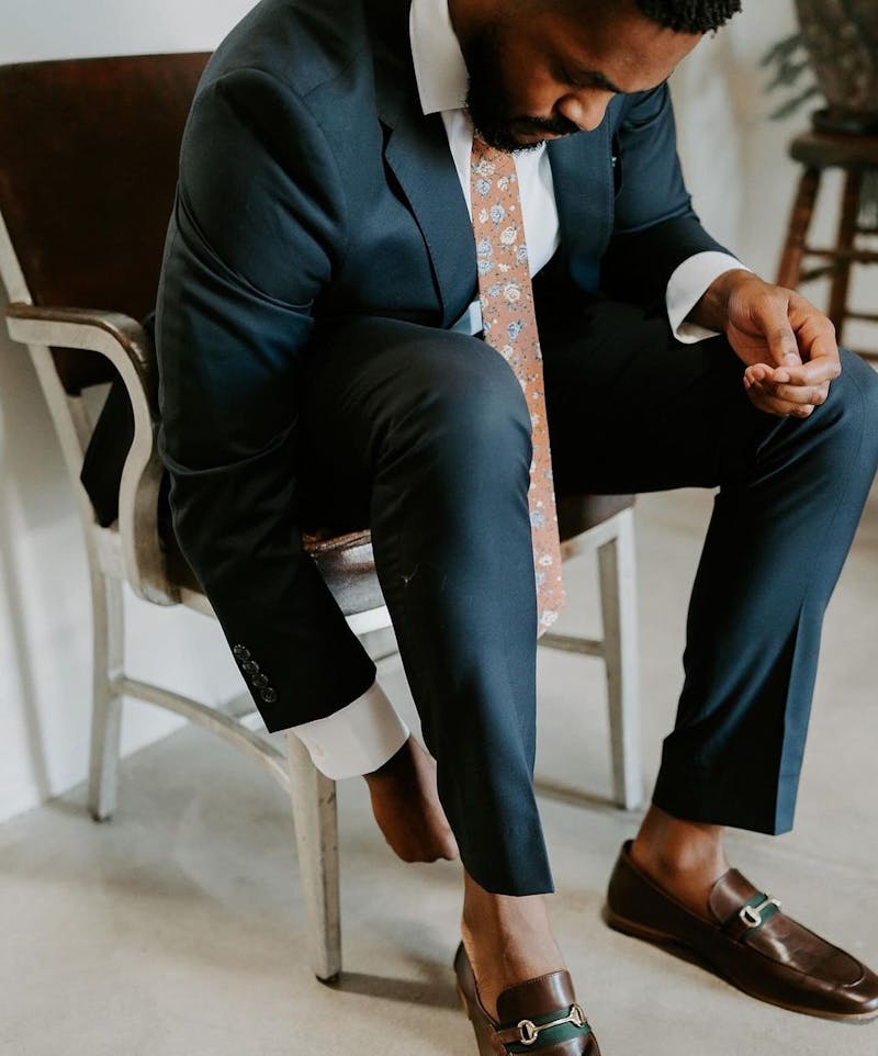 Getting ready in wedding guest outfit wearing navy blue suit for men, floral tie, and brown loafers.