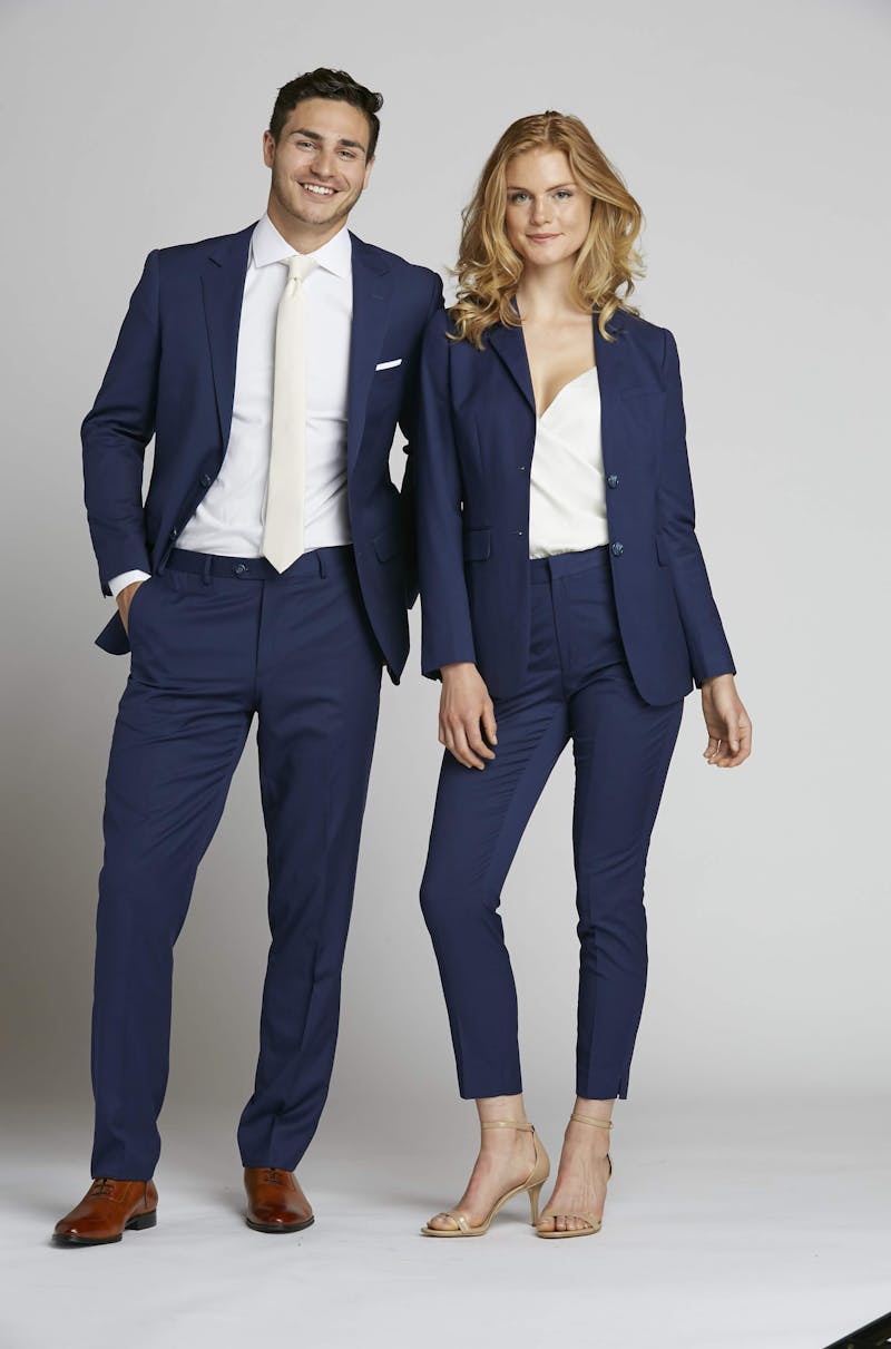 Navy blue wedding guest suits for men and women styled with white accessories for semiformal dress code