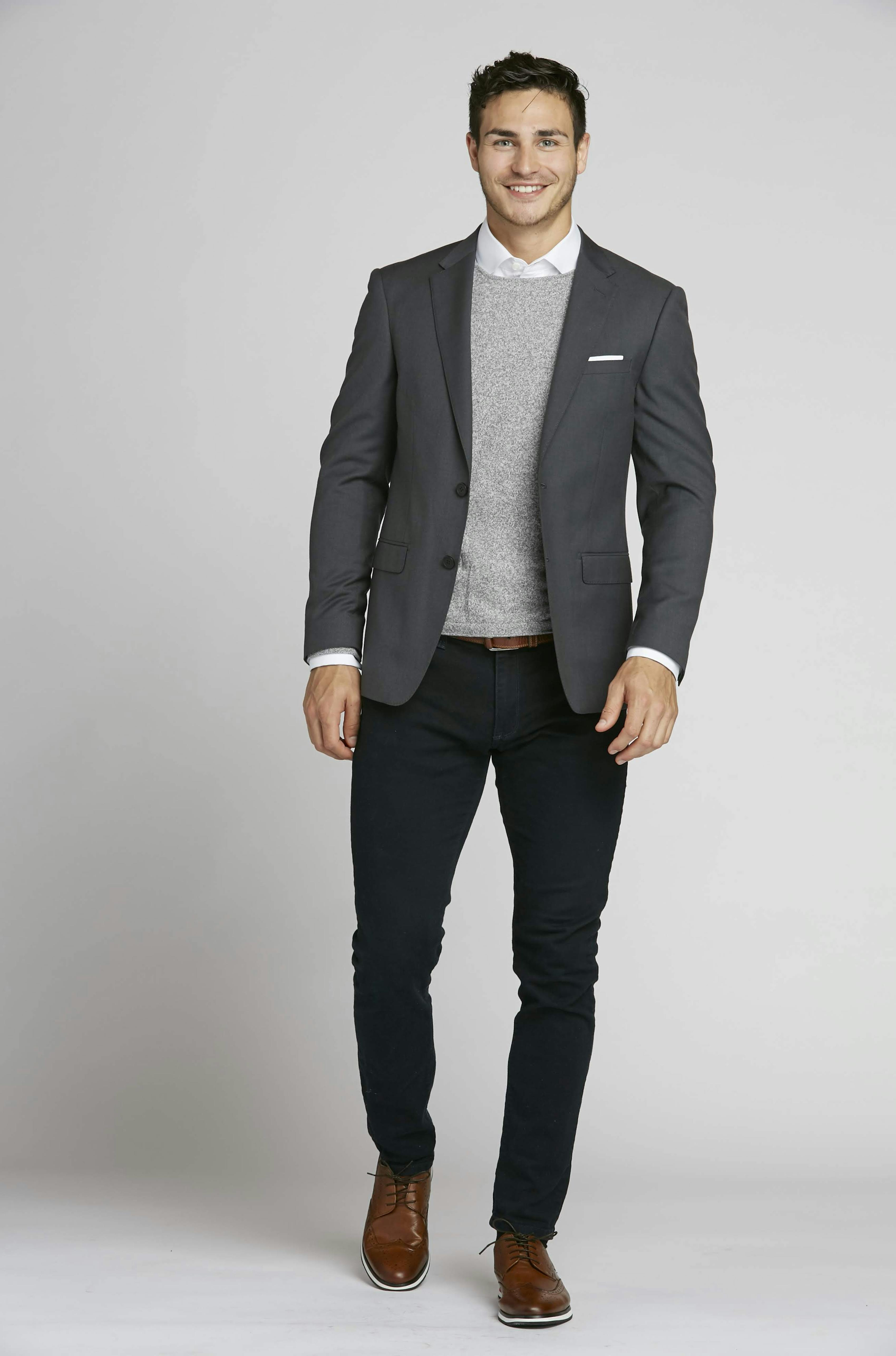 Man wearing suit separates for business casual office dress code with blazer, sweater, and jeans.