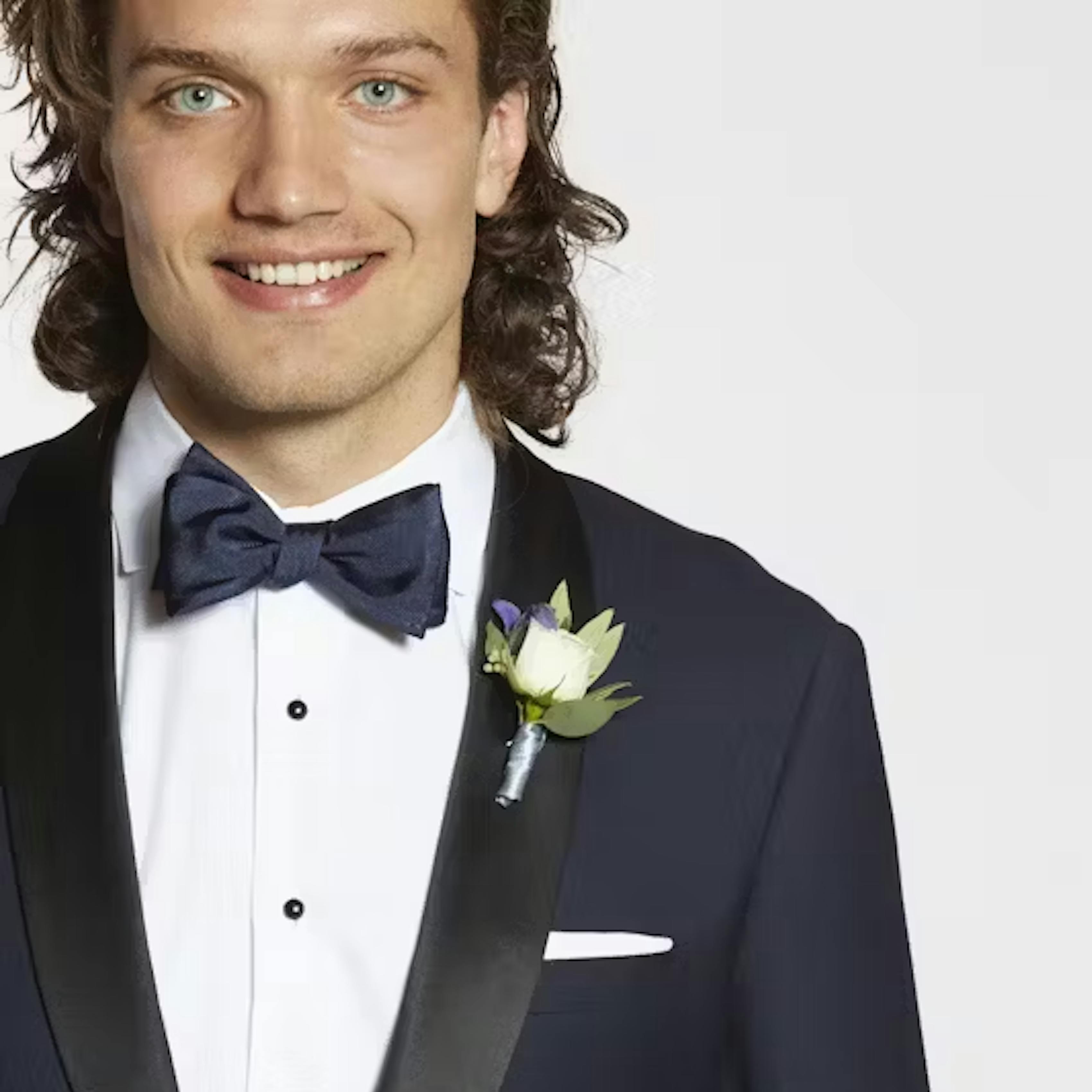 Man dressed for black tie event showing how to pin a boutonniere on a shawl lapel tuxedo