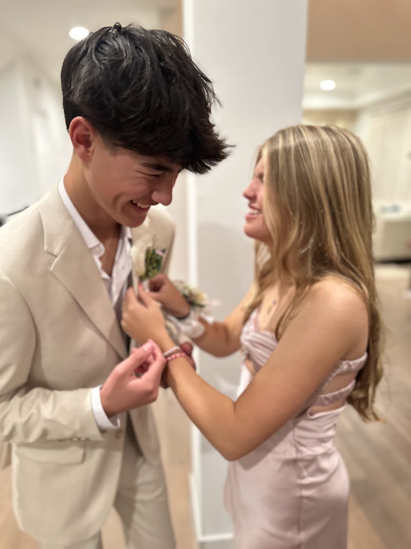 High school couple pinning on boutonniere for prom to a tan suit