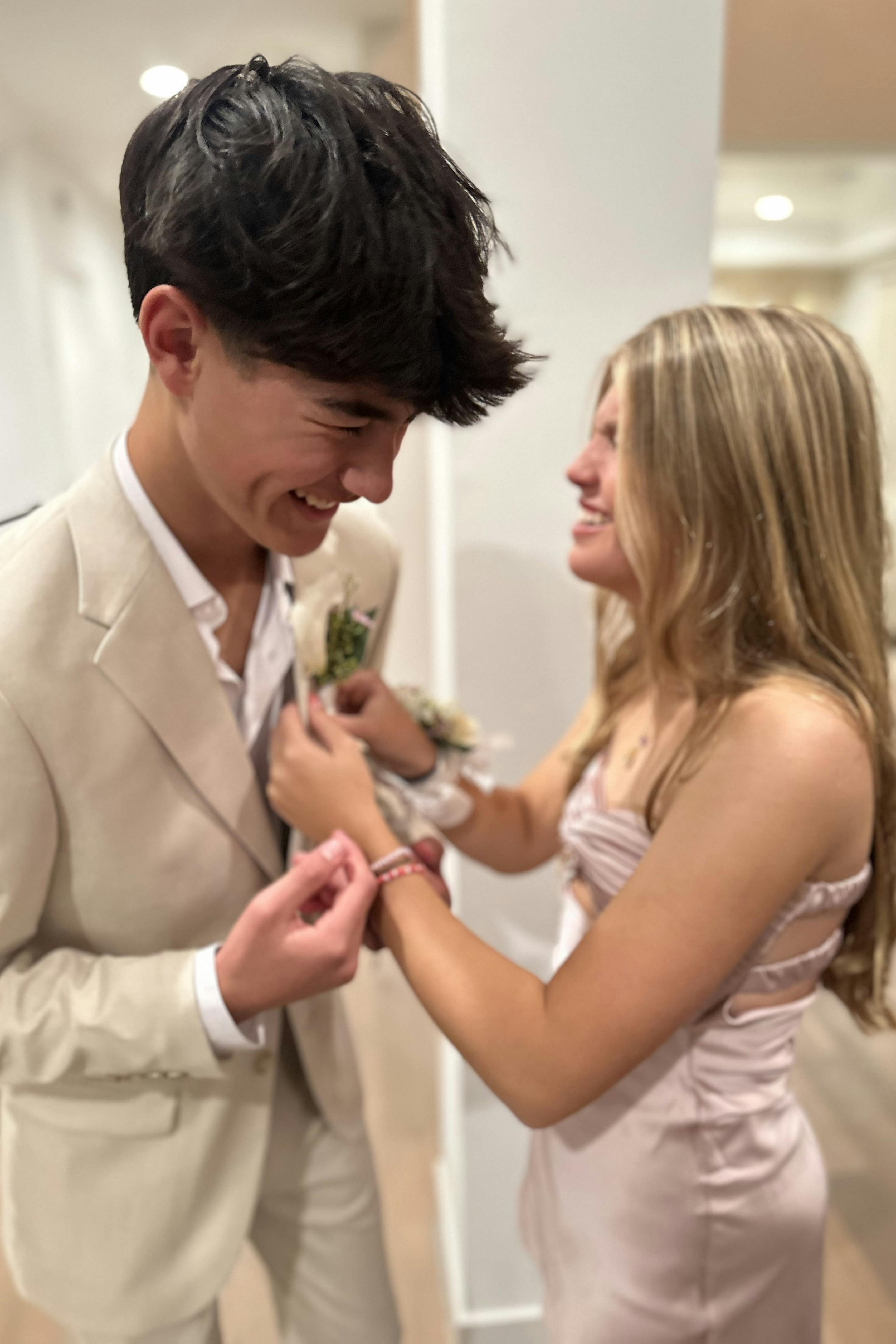 High school couple pinning on boutonniere for prom to a tan suit