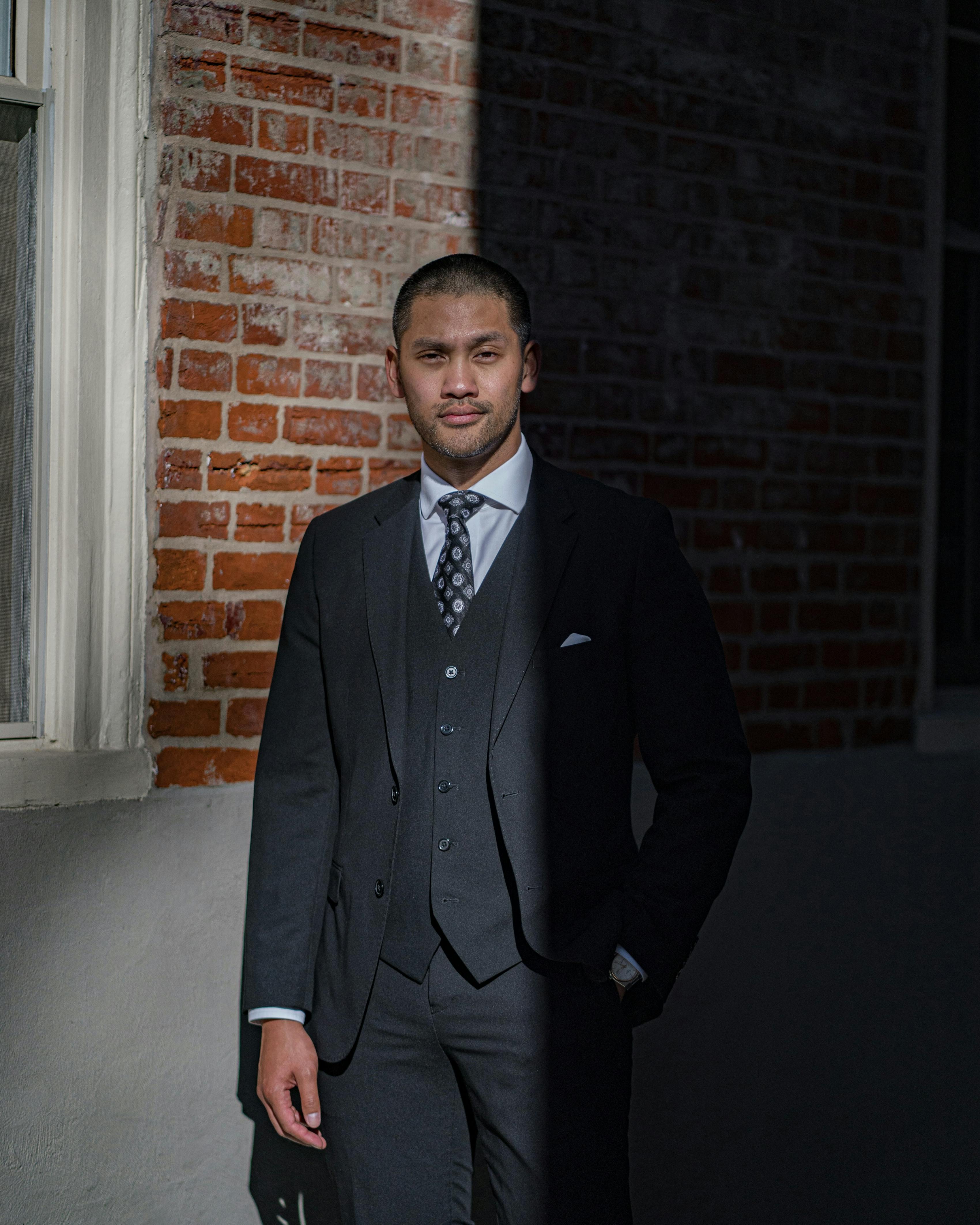 Man wearing business professional suit with 3-piece styling, a dark patterned tie, white dress shirt, and pocket square.