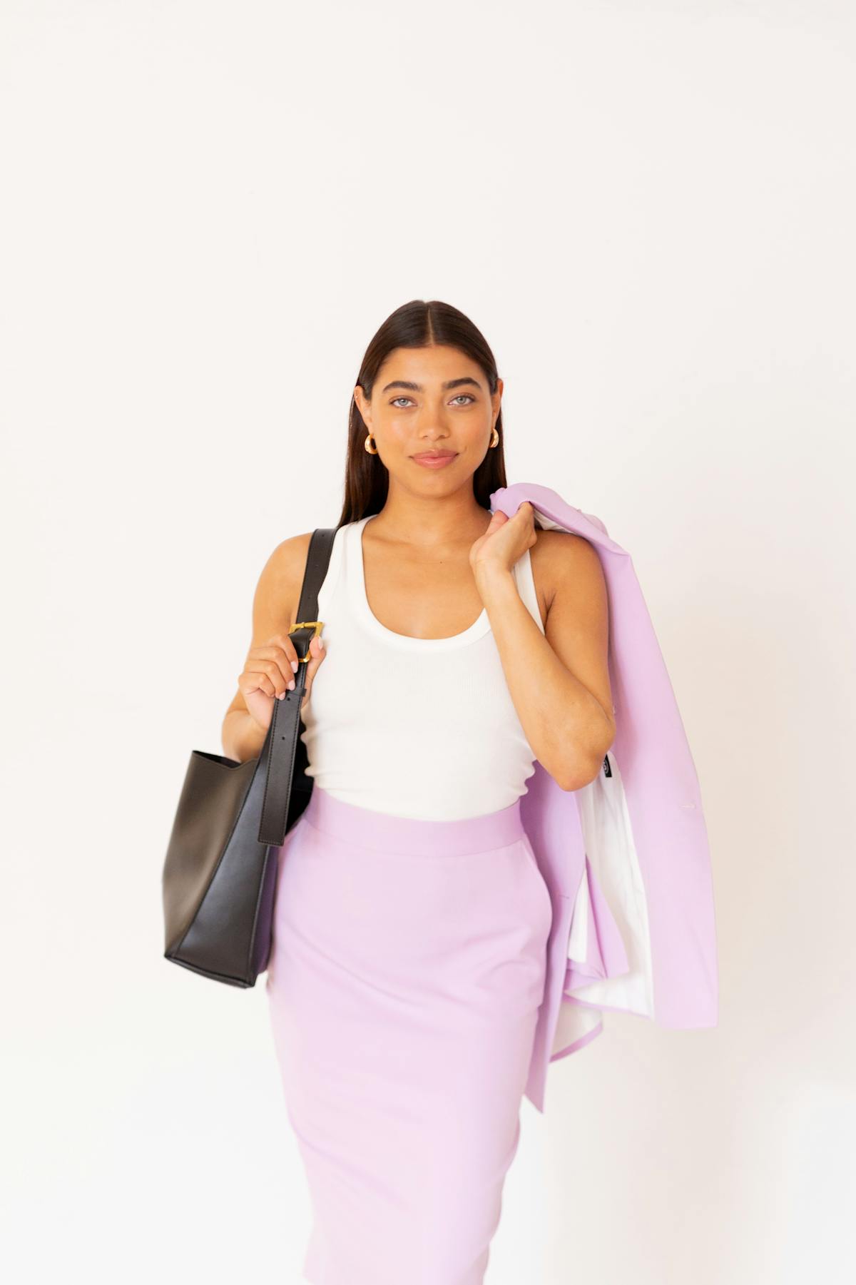 Woman wearing stylish trendy office outfit in purple suit skirt set, tank top, and a leather work bag