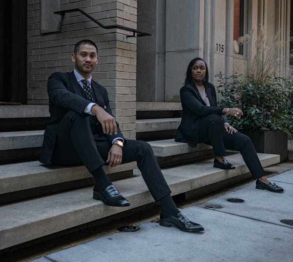 A man and a women in dark suits for professional outfits sitting on office steps showing off dress shoes.