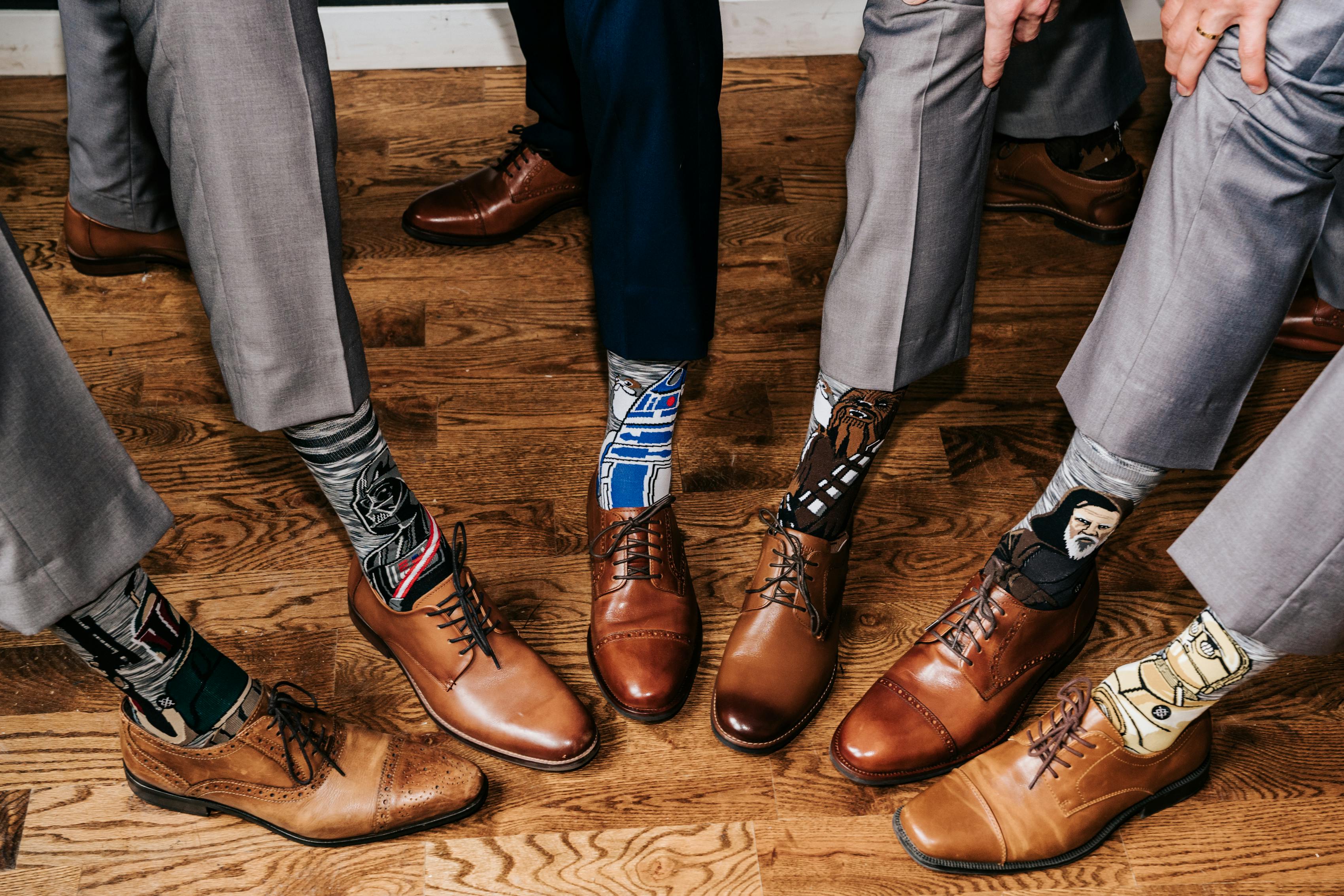 6 men posing their light brown and tan shoes with grey suit pants and funny socks in a circle