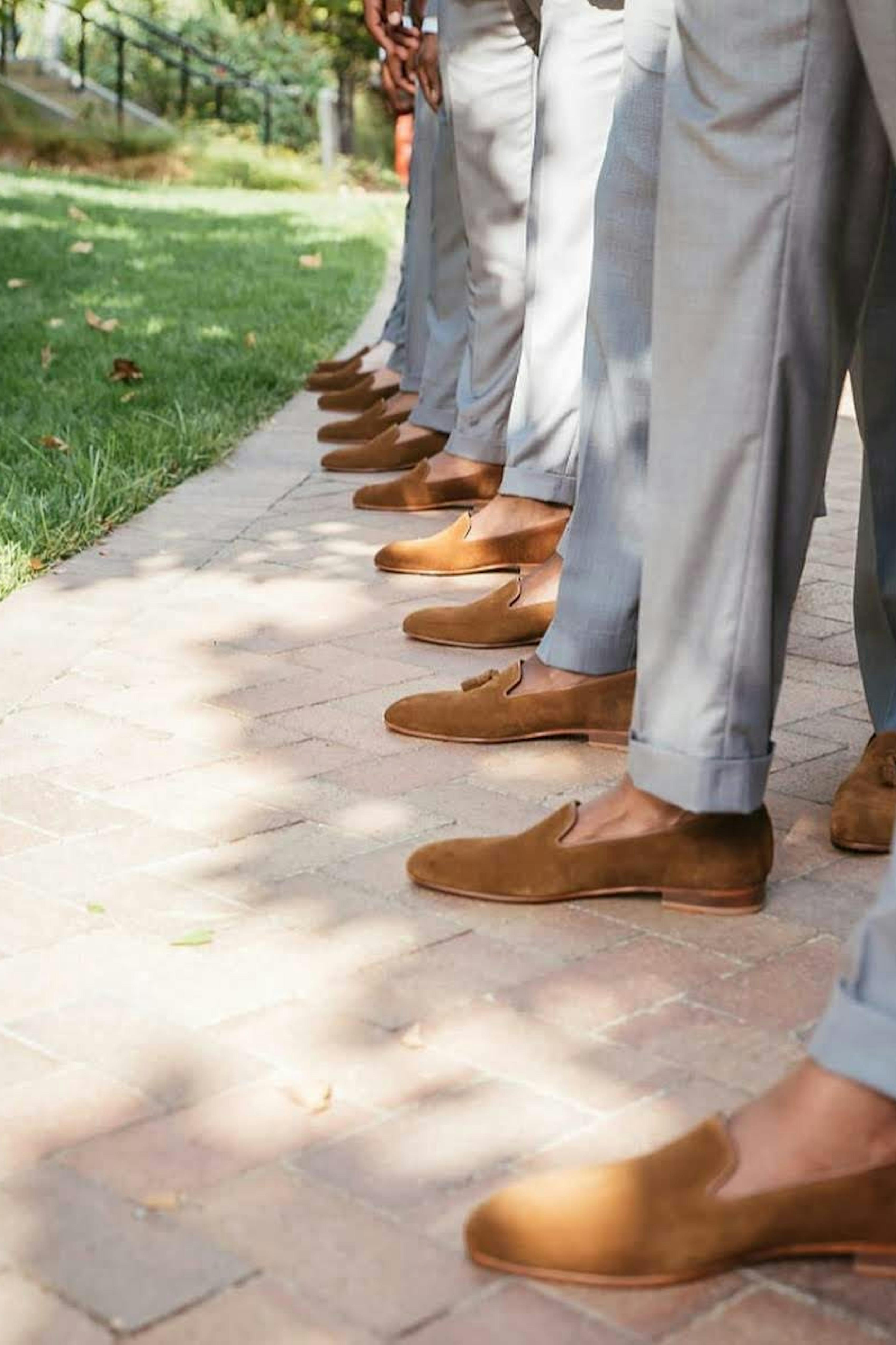 Group of groomsmen showing off slip on suede light brown loafers with light grey suit pants
