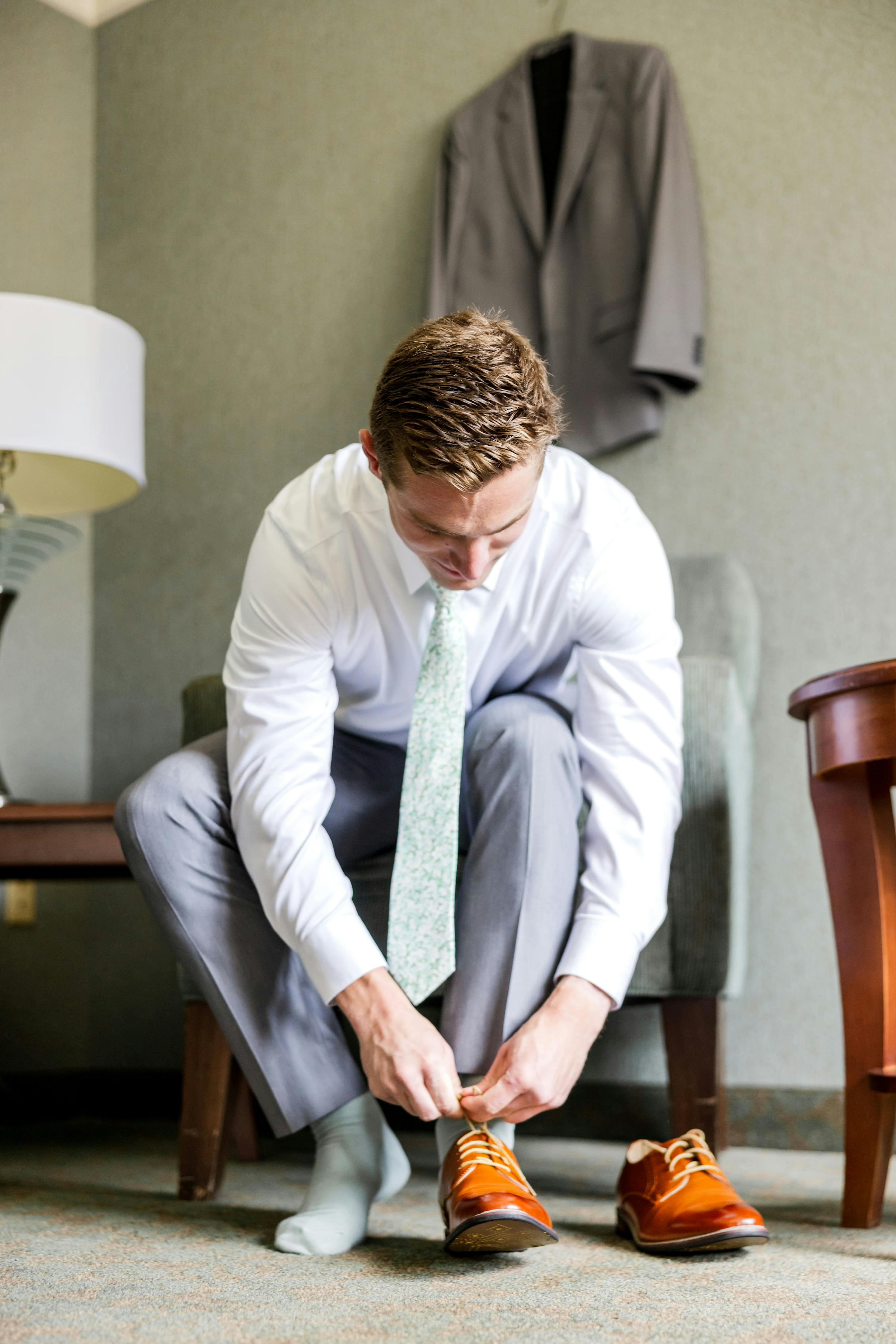 Groom getting ready putting on brown shoes with light grey suit for wedding