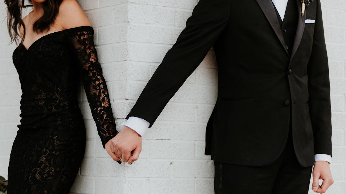 Black lace dress and black tuxedo for formal wedding guest attire.