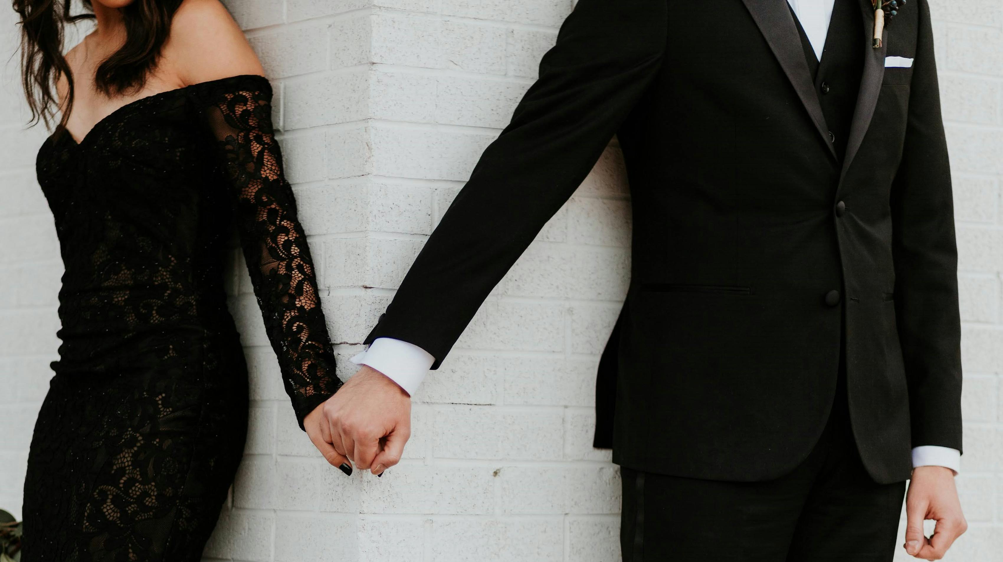 Black lace dress and black tuxedo for formal wedding guest attire.