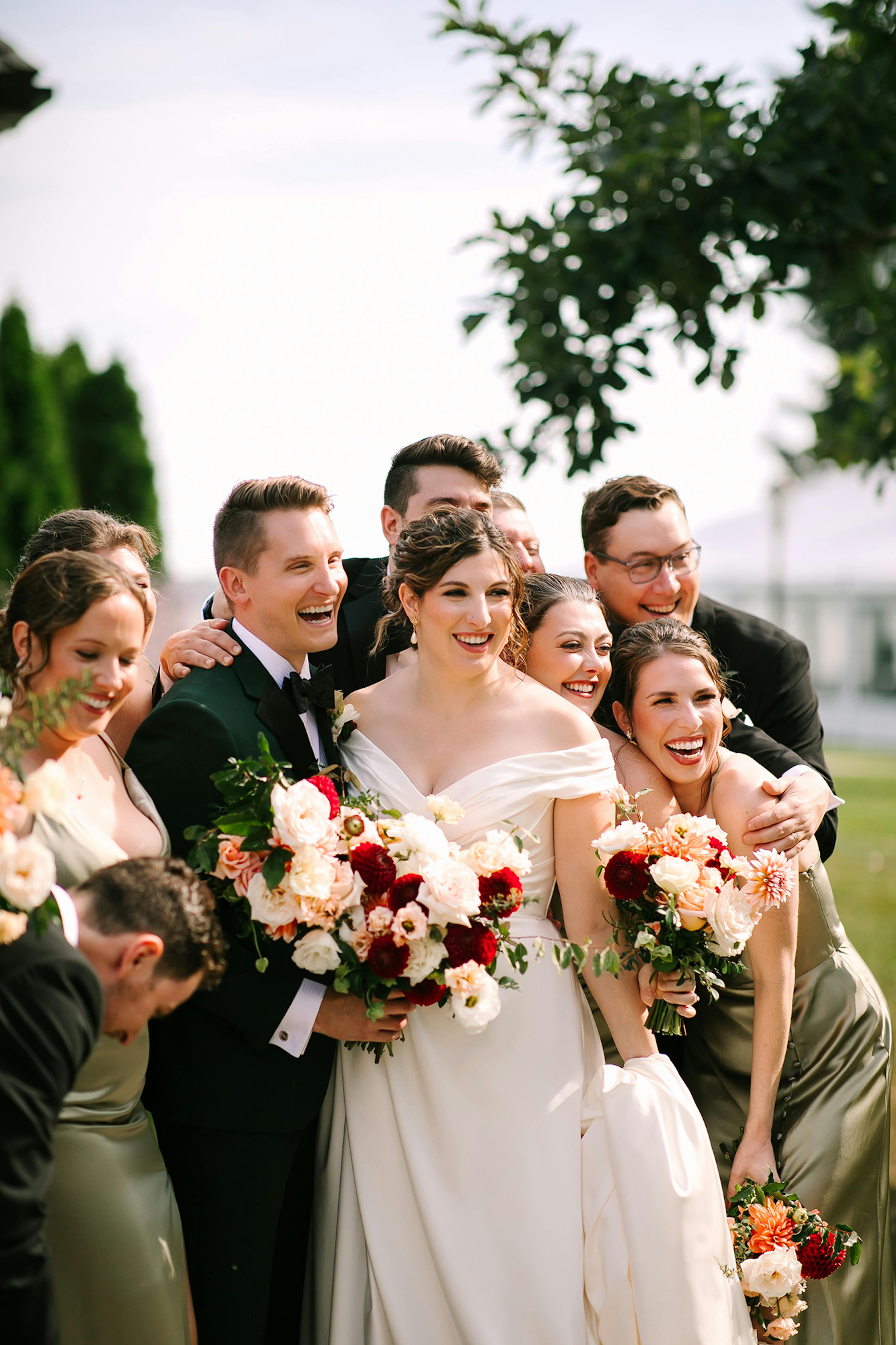 Wedding party gathered together showcases their bridal bouquets of white, peach, and burgundy flowers.