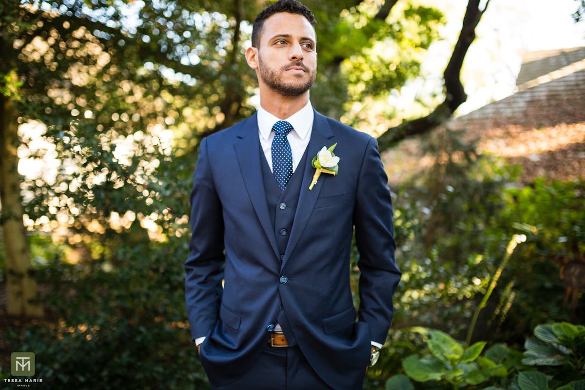 Man dressed in a 3 piece navy suit for a funeral with a white boutonnière and a patterned navy tie 