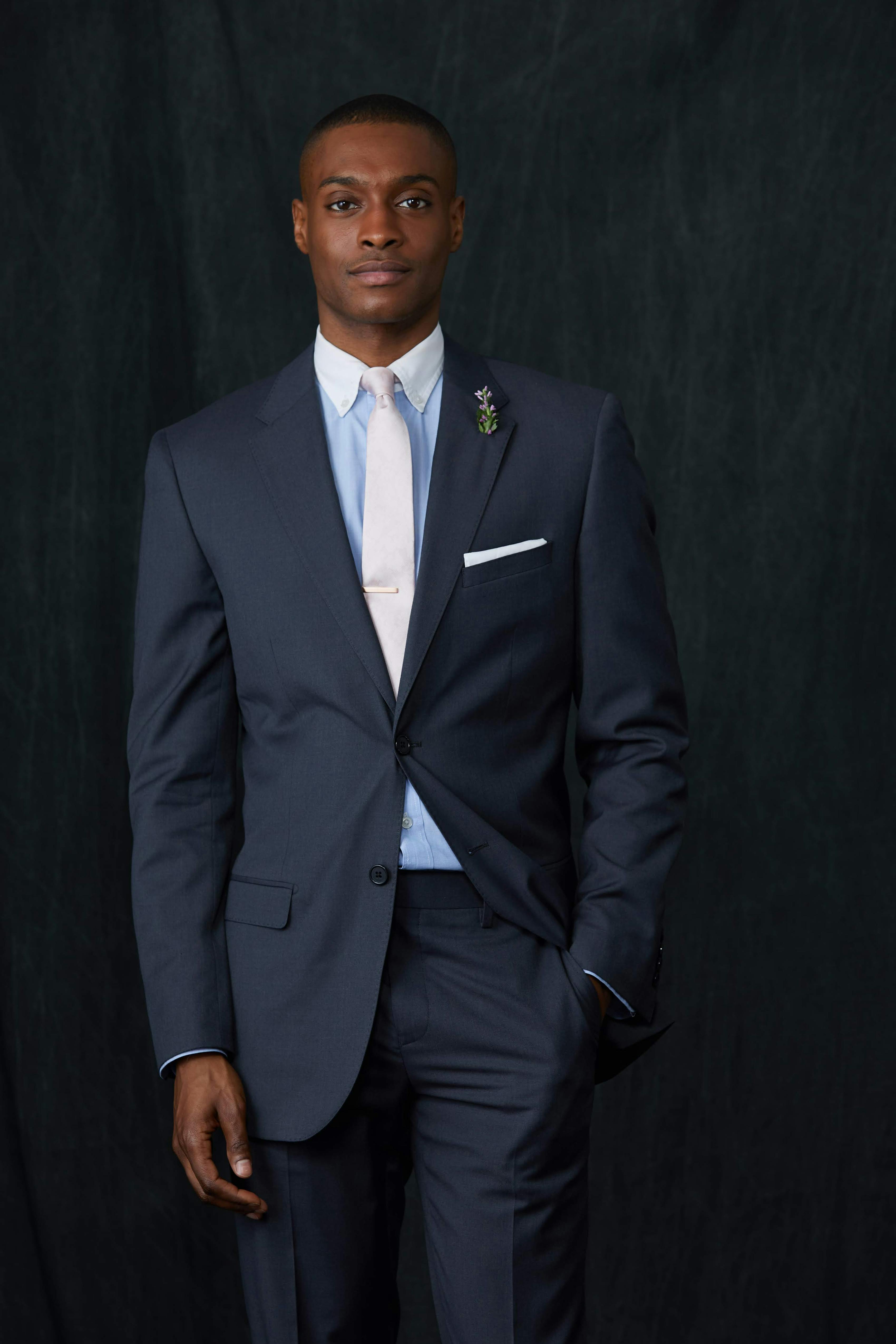 Men's funeral outfit with a charcoal grey suit, light pink tie, and light blue dress shirt.