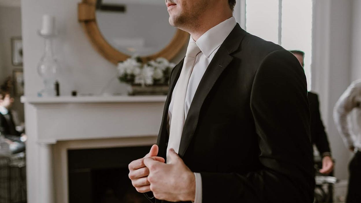 Men's black suit with white shirt and white tie for funeral attire.