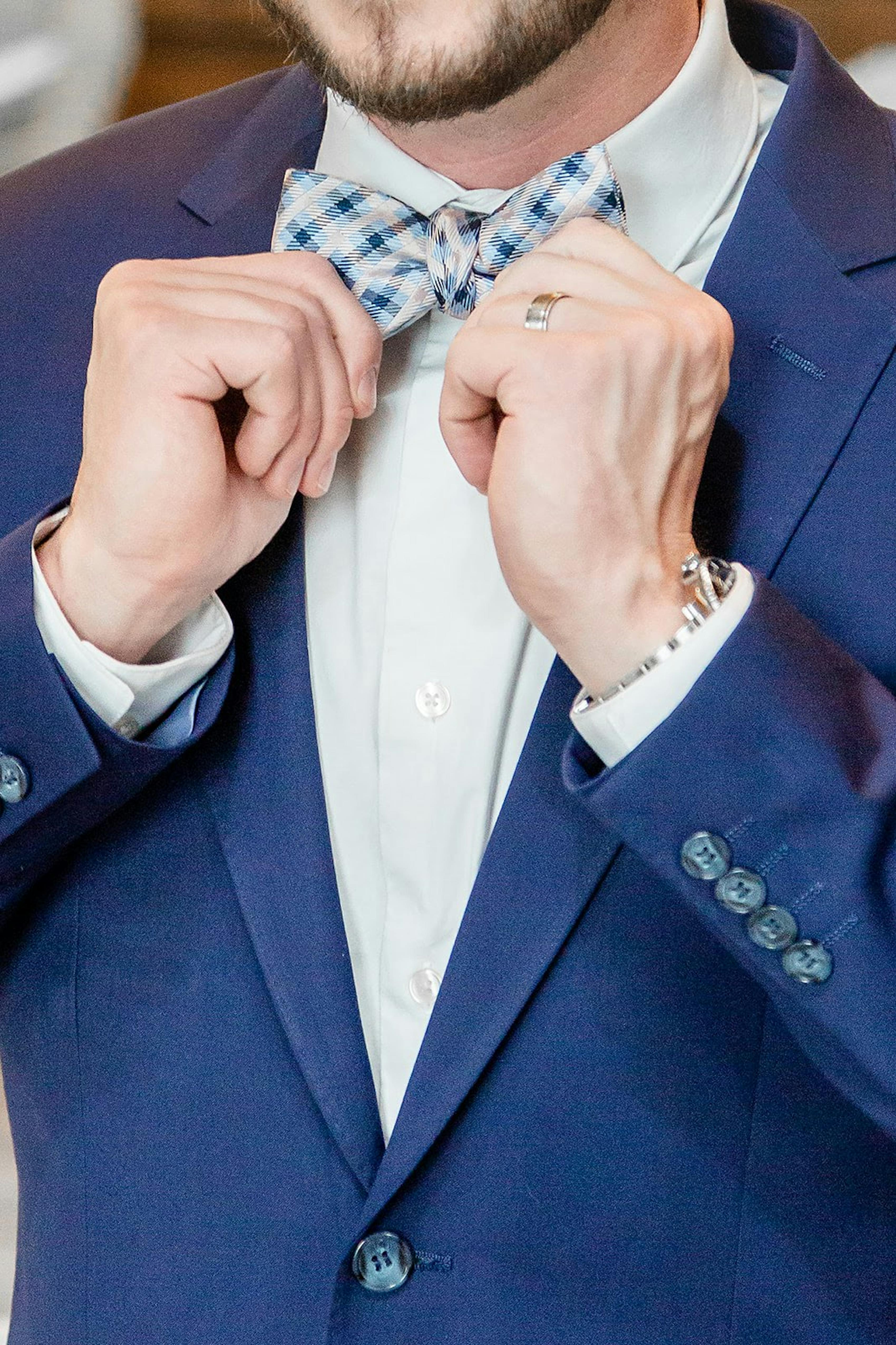 Man adjusting blue and grey checkered bow tie for cocktail wedding