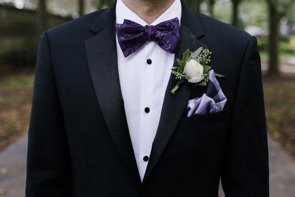 Men's black tuxedos with pocket square and purple paisley bow tie for a formal attire event
