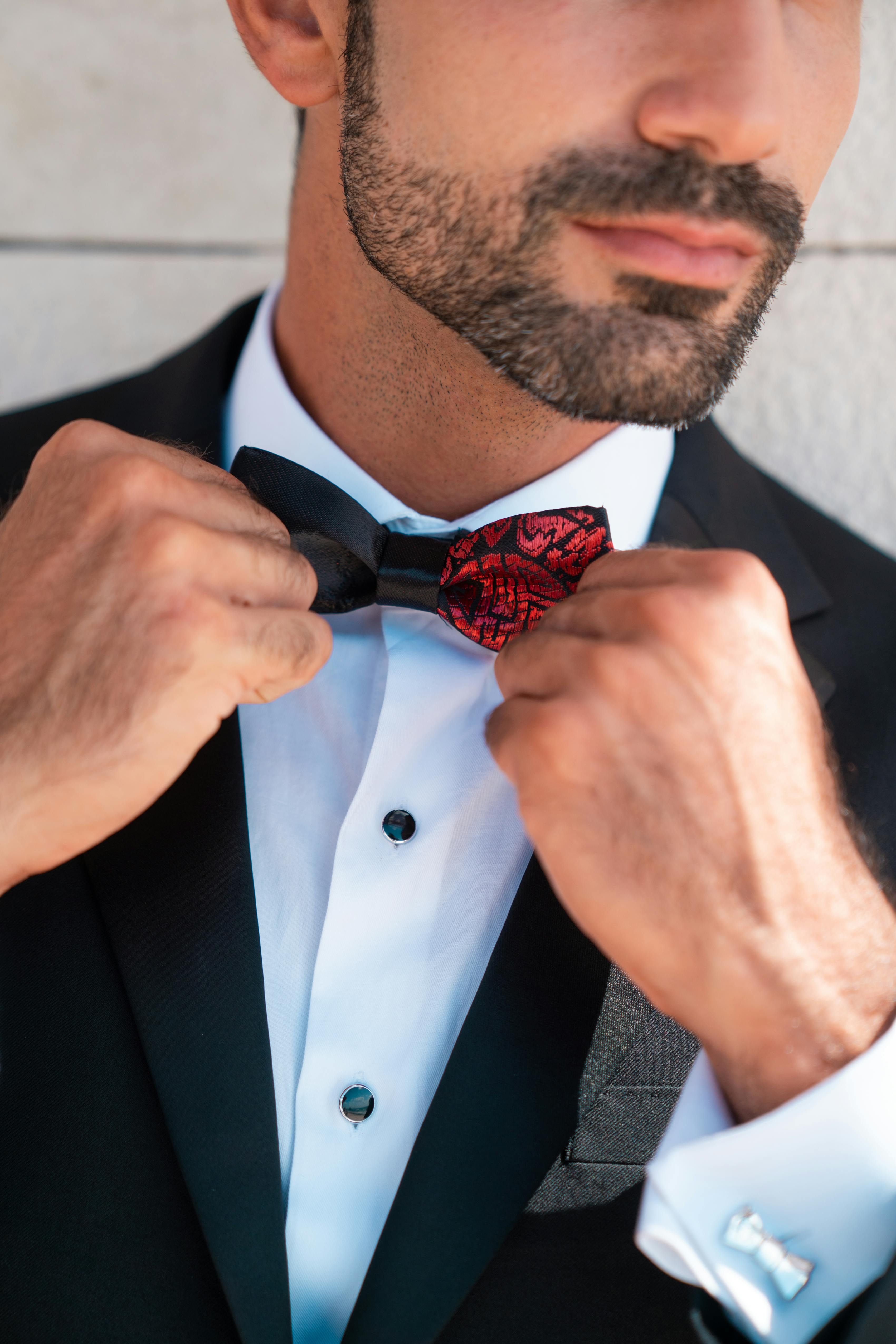 Man adjusting black and red printed bow tie with a tuxedo and cufflinks for a black tie event.