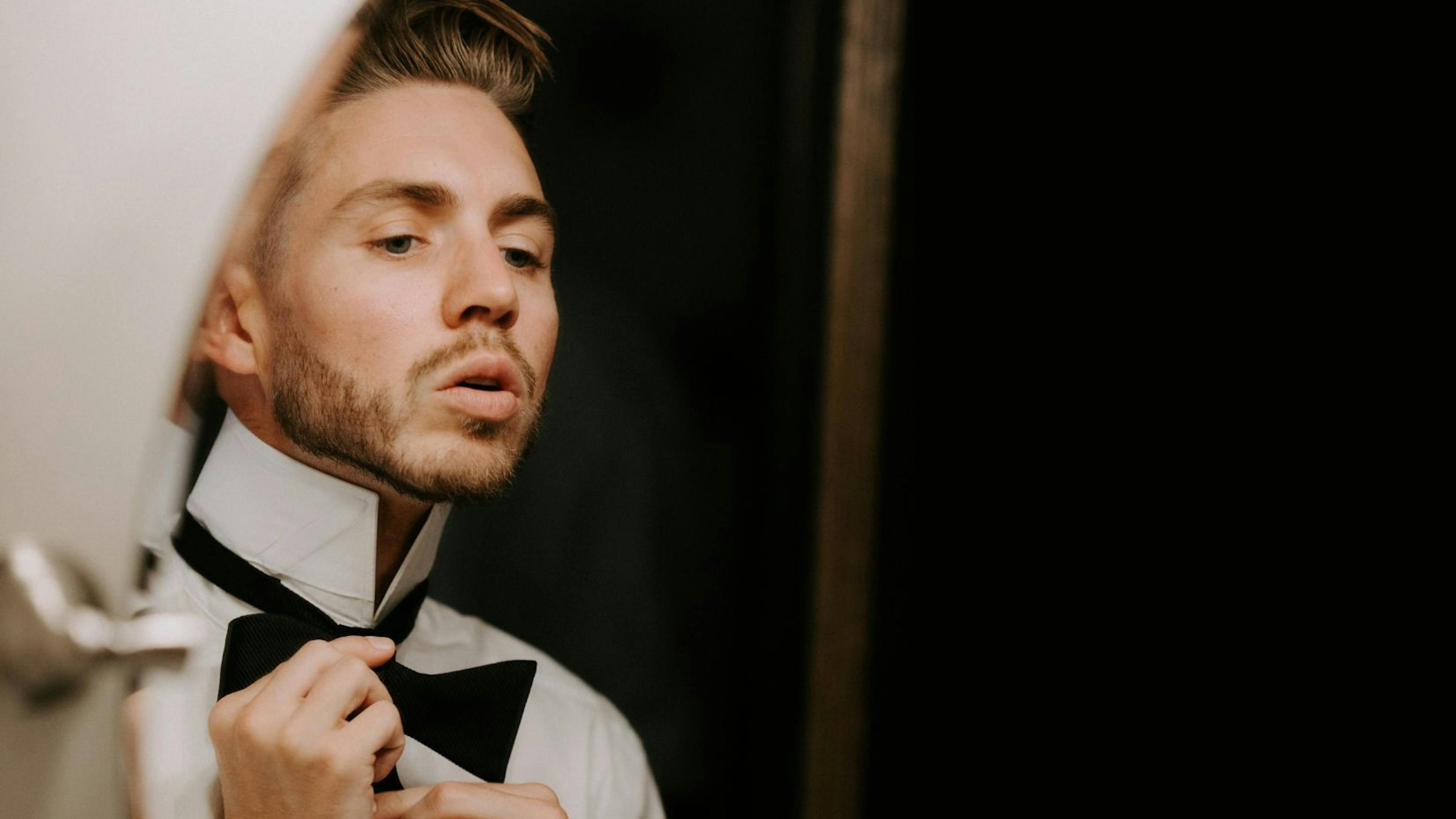 Man tying black bow tie in the mirror