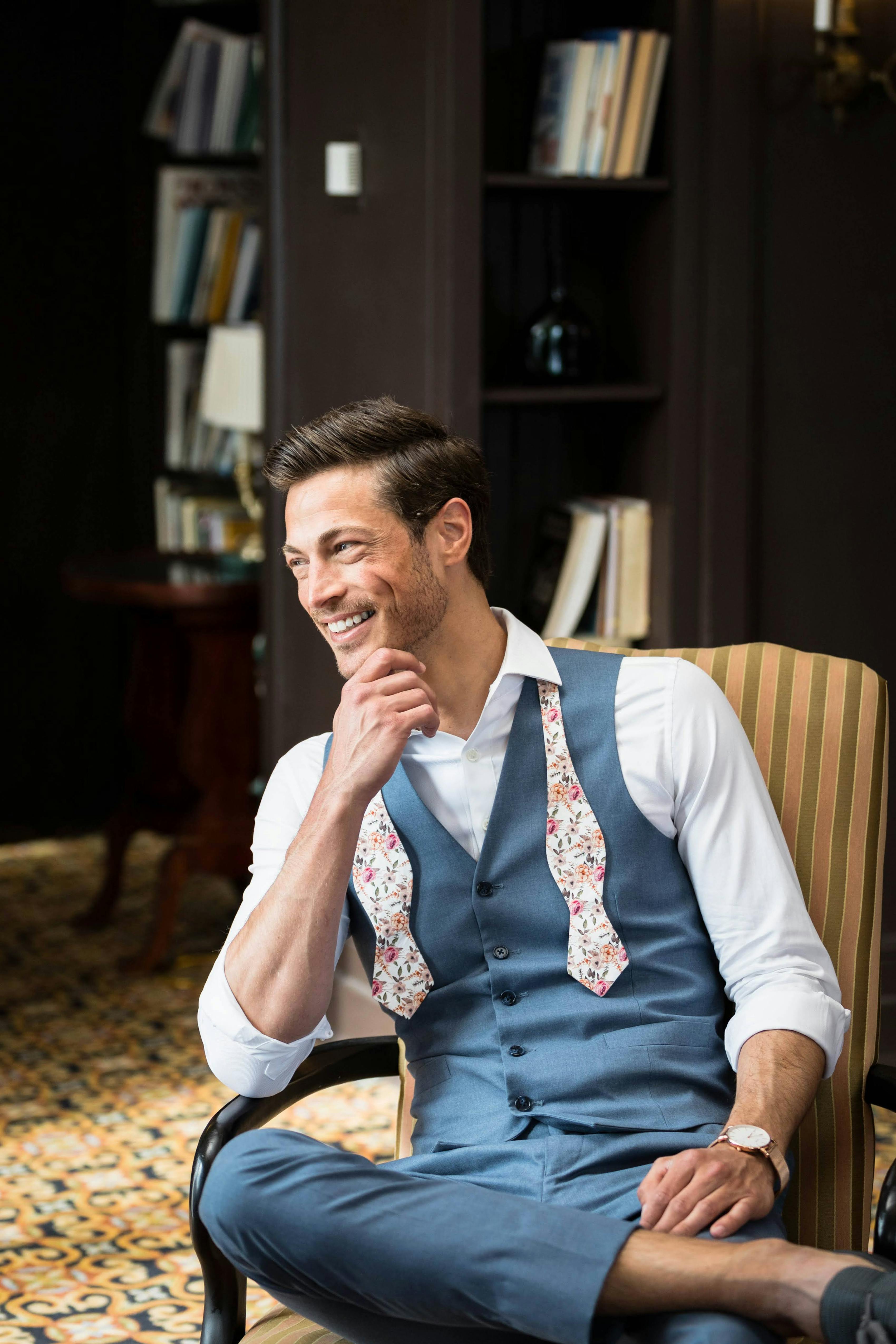 Man laughing wearing light blue suit vest and suit pants with pink floral bow tie