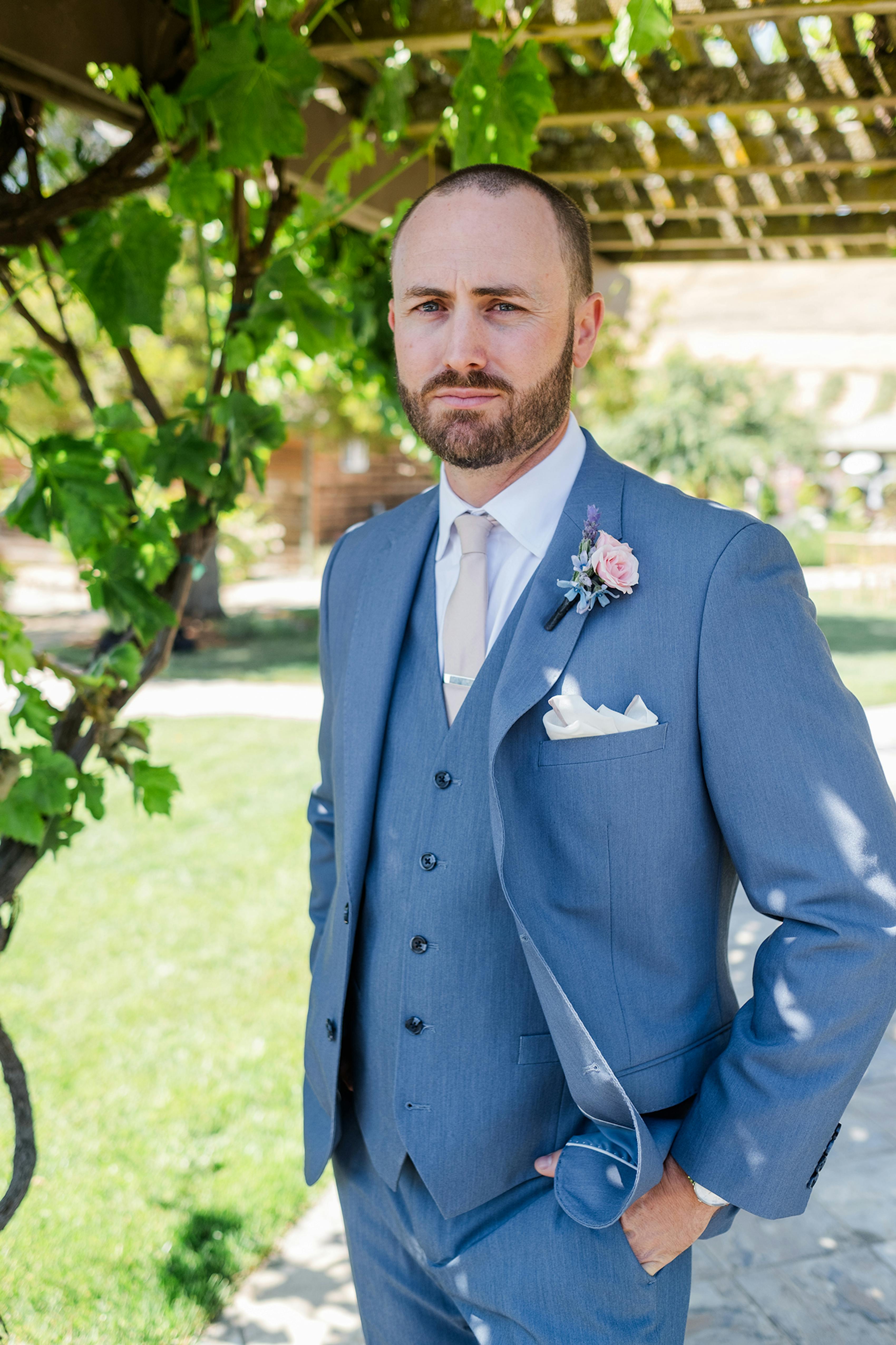 Groom in a dusty blue wedding suit and blue suit vest with tan tie and pocket square.