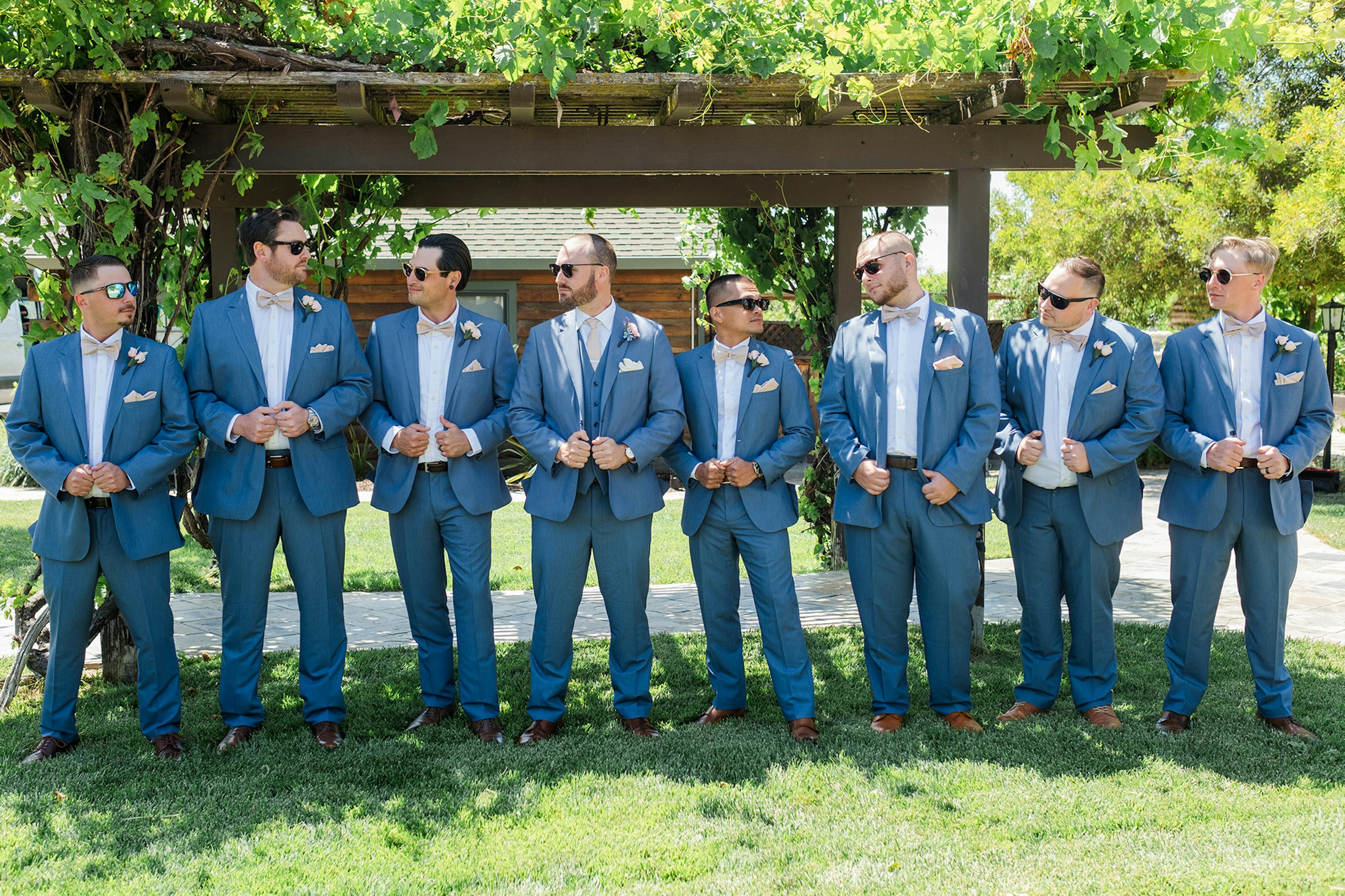 Group of groomsmen wearing light blue wedding suits and tan bow ties.
