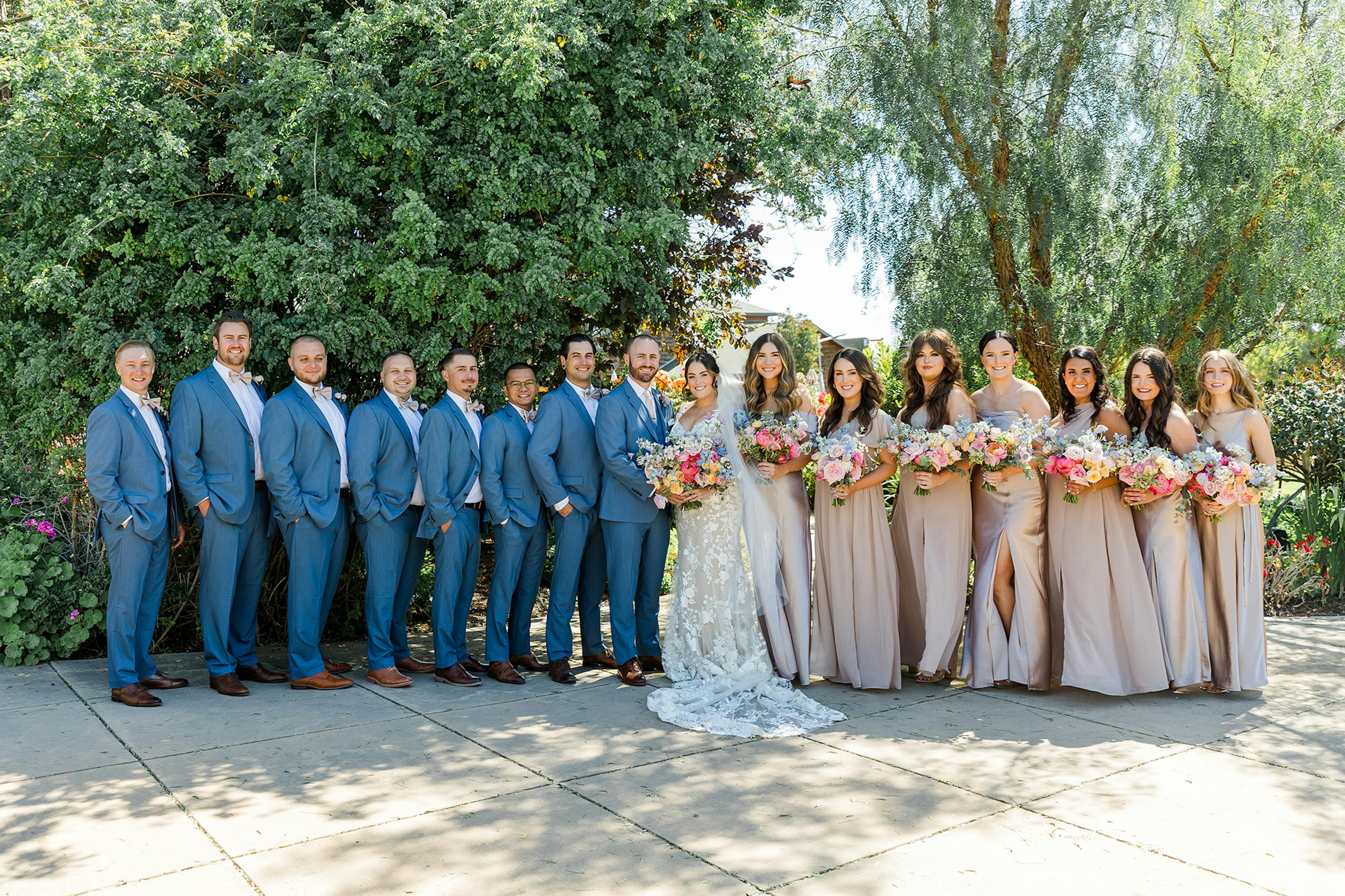 Group dressed for a spring wedding in blue wedding suits and neutral bridesmaids dresses with bold bridal bouquets.