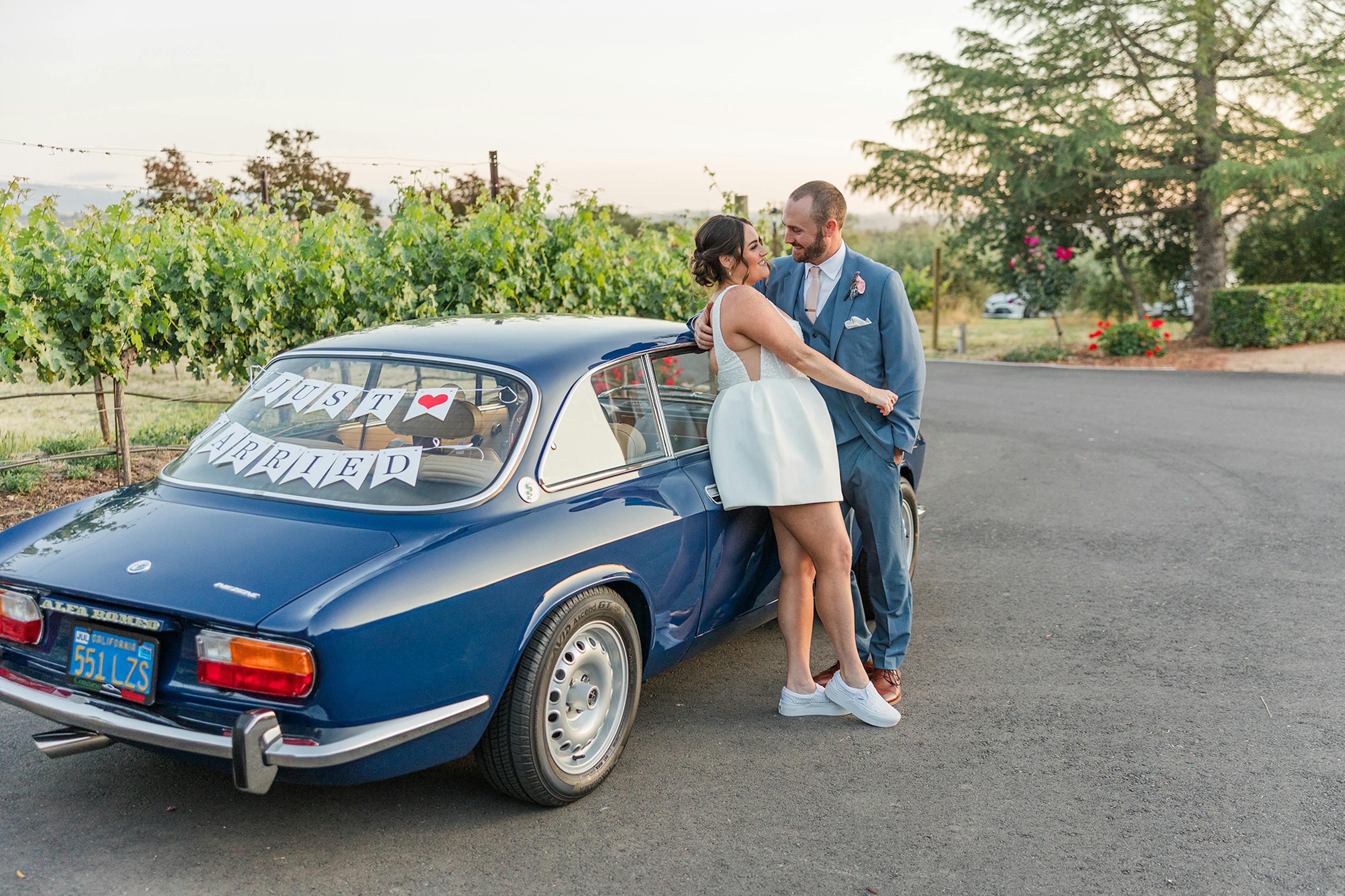 Bride's white short after party dress next to wedding getaway car with just married sign.
