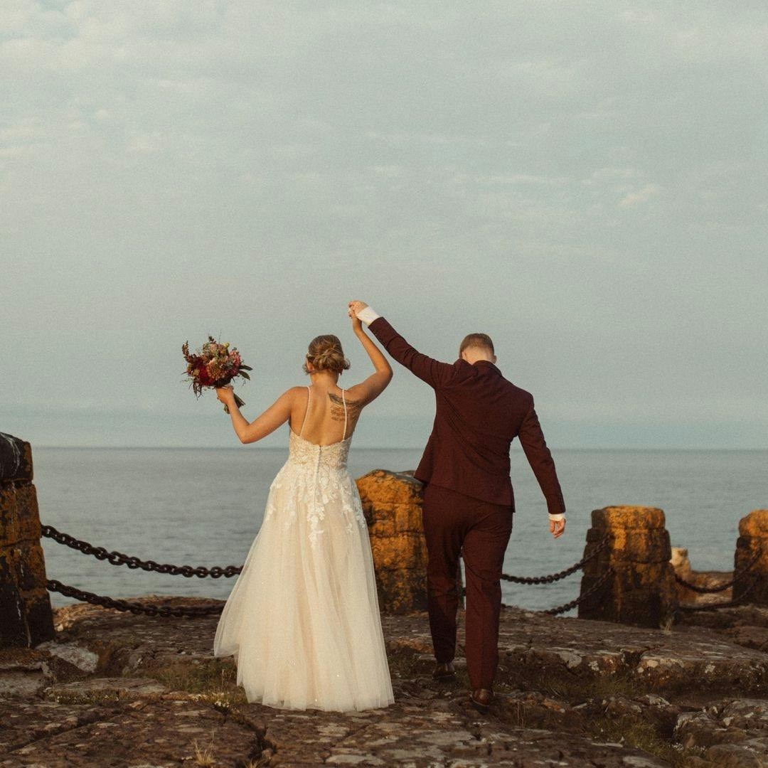 Seaside wedding with a lacy pink wedding dress and burgundy wedding suit for women